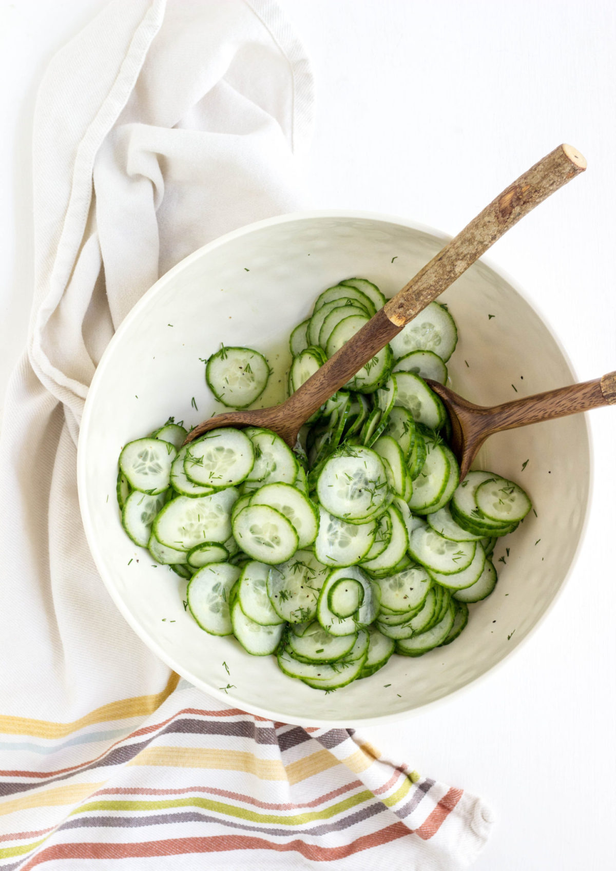 Overhead view of sliced cumbers in a bowl tossed with vinegar and dill. 