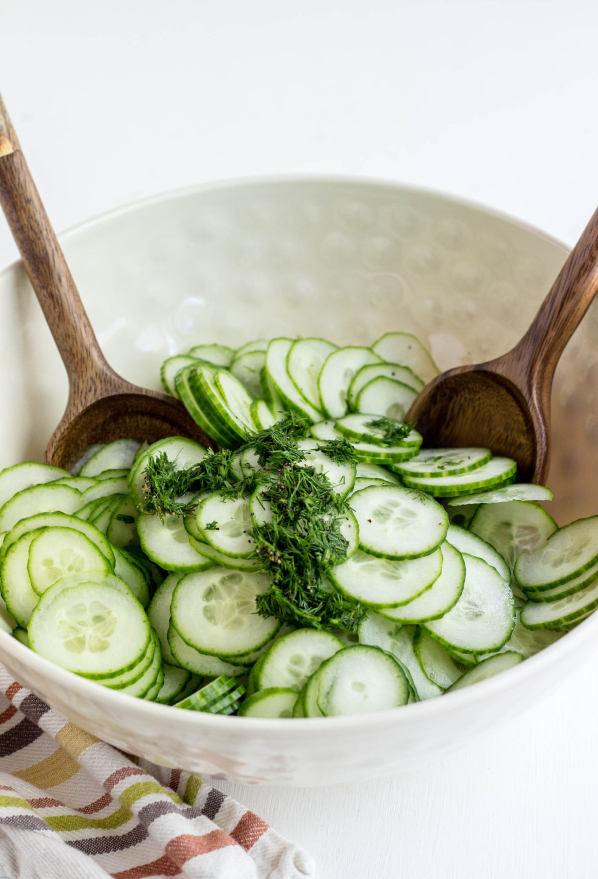 Sliced cucumbers in a bowl with chopped fresh dill. 