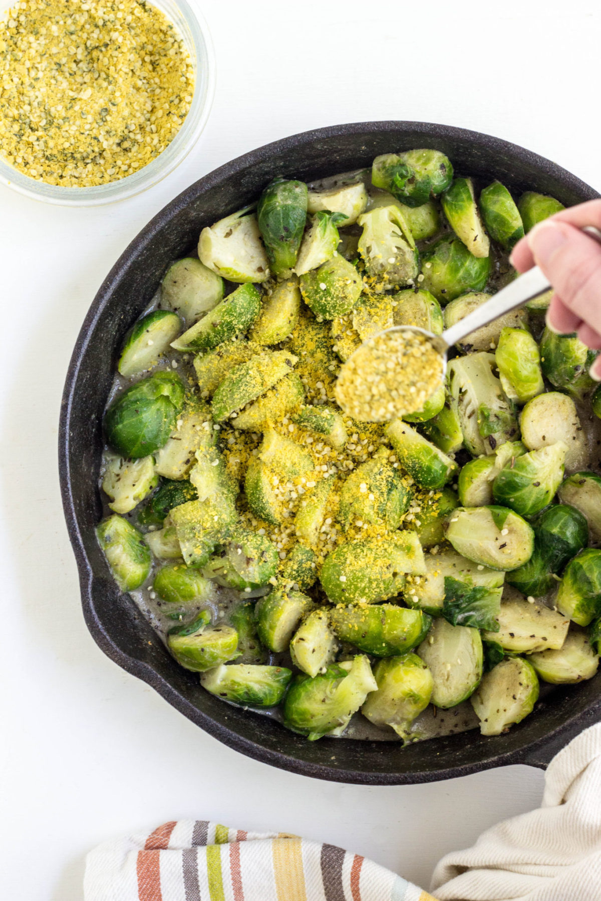 Top view of Brussels Sprouts Gratin being sprinkled with vegan parmesan prior to baking.  