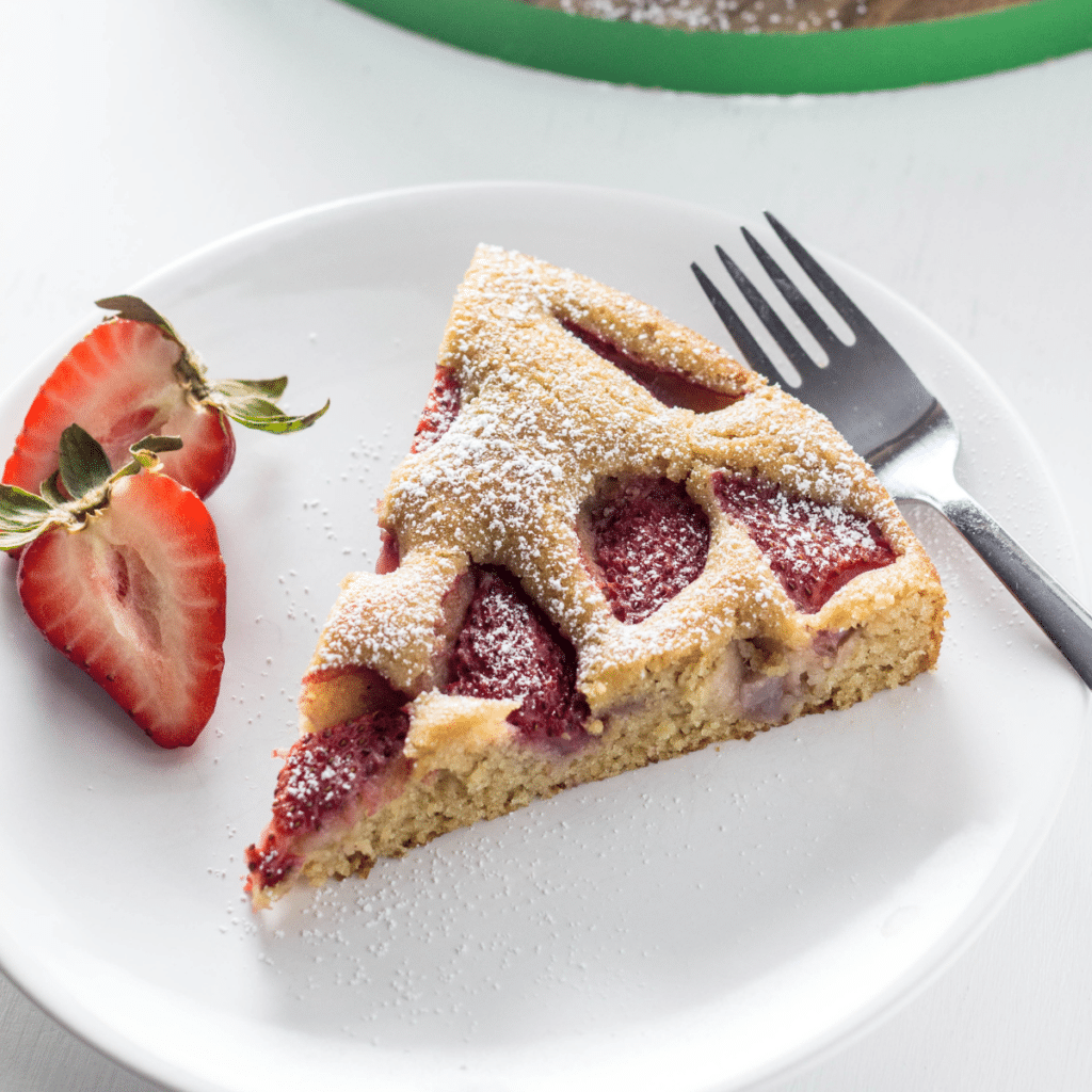 Side view of a slice of Vegan Berry Skillet Cake on a white plate with strawberry slices on the side.