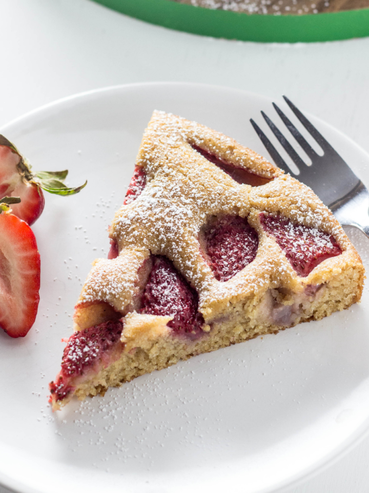 Side view of a slice of Vegan Berry Skillet Cake on a white plate with strawberry slices on the side.