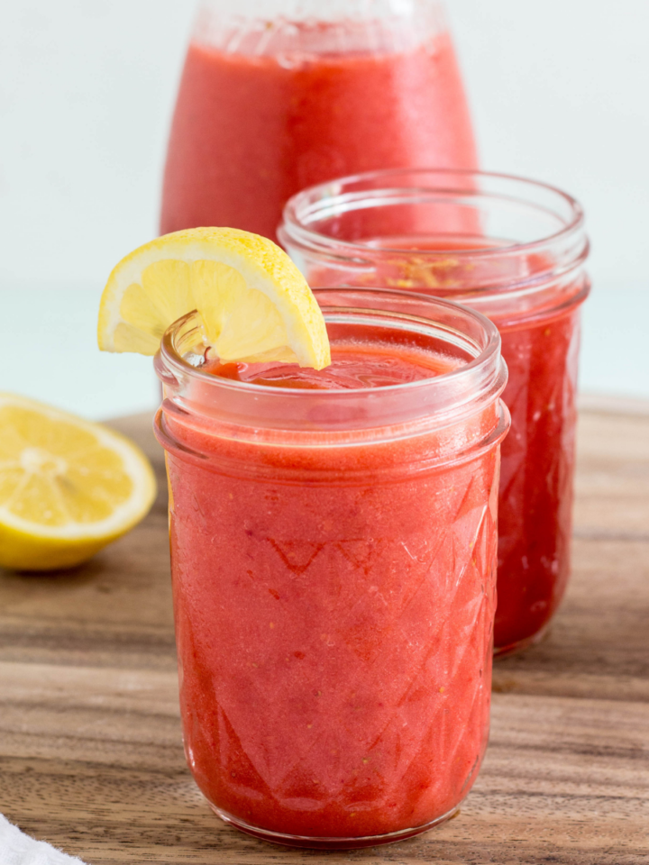 Close up side view of Frozen Strawberry Lemonade in a glass with a lemon wedge on the rim.