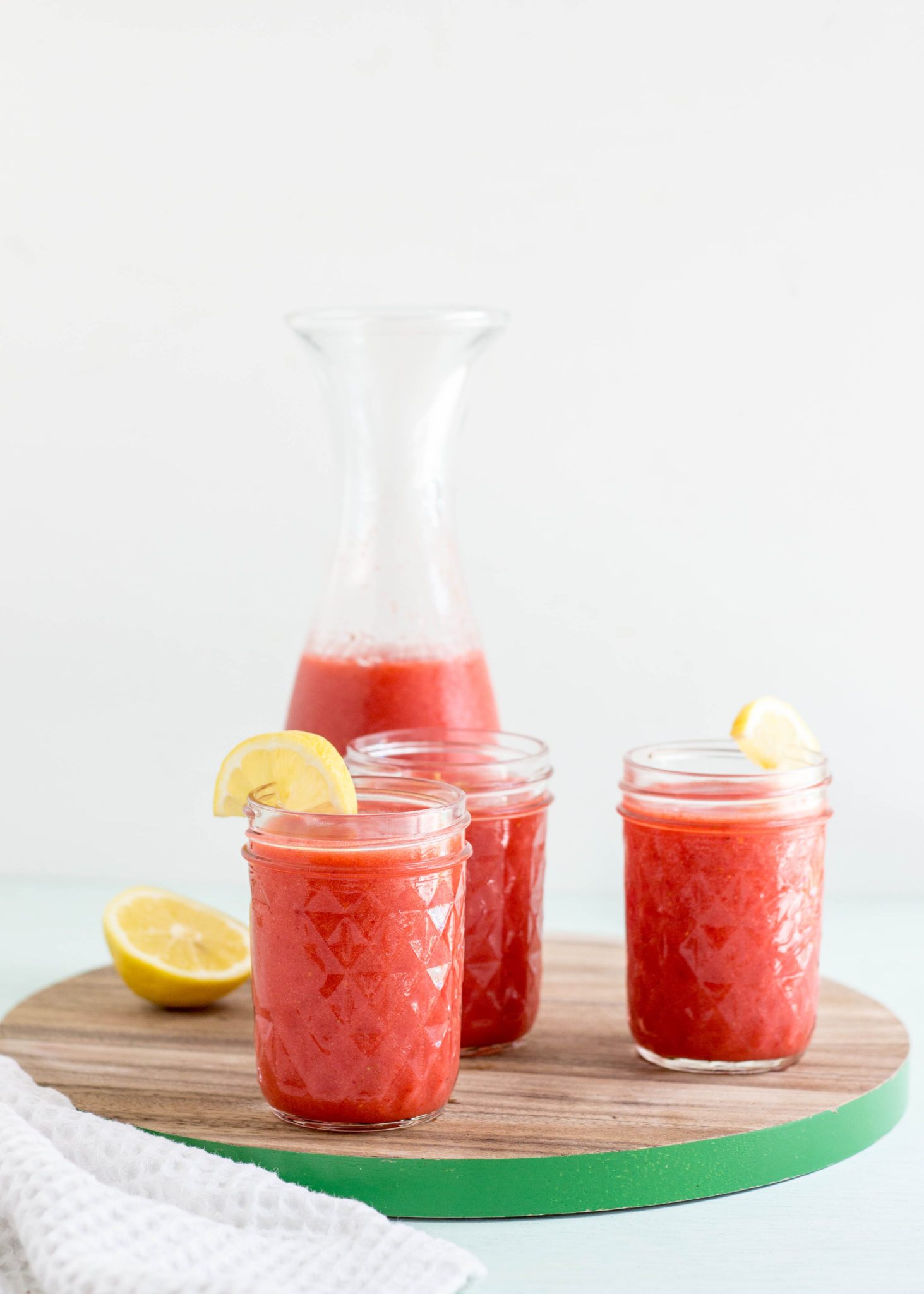 Side view of three glasses and carafe of Frozen Strawberry Lemonade. 