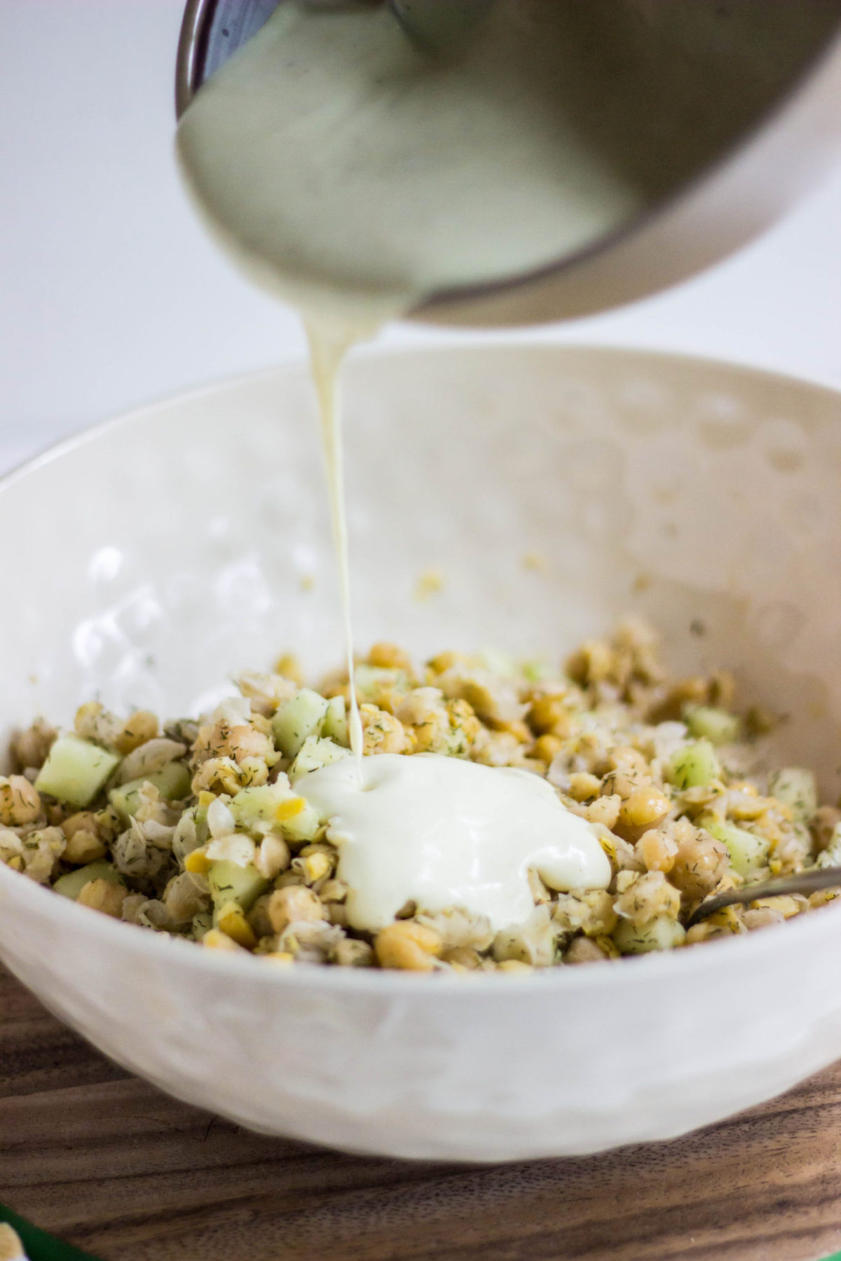 Side view of yogurt dressing being poured onto chickpea salad. 