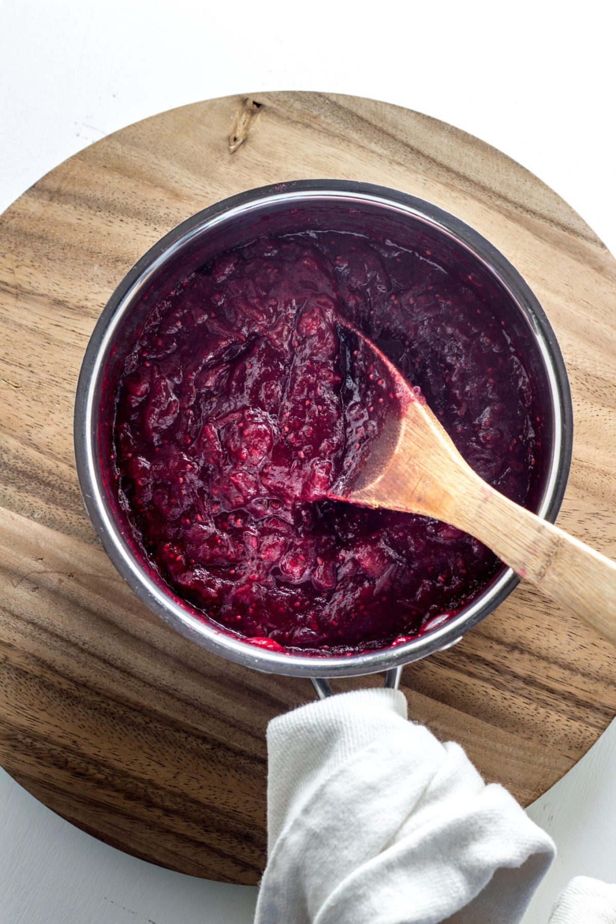 Top view of jam in a pot with a wooden spoon sitting on top of a wooden board. 