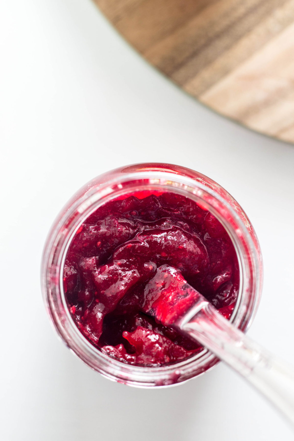 Close up top view of a jar of Simple Cranberry Orange Jam with a knife resting in it. 