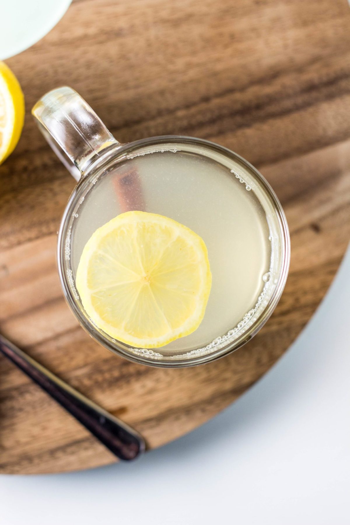 Top view of tea in a mug with a lemon slice and cinnamon stick on a wooden cutting board.