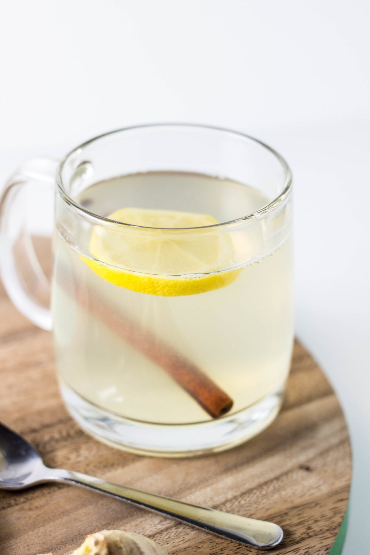 Side view of Ginger Lemon Tea in a clear mug with a slice of lemon and cinnamon stick.