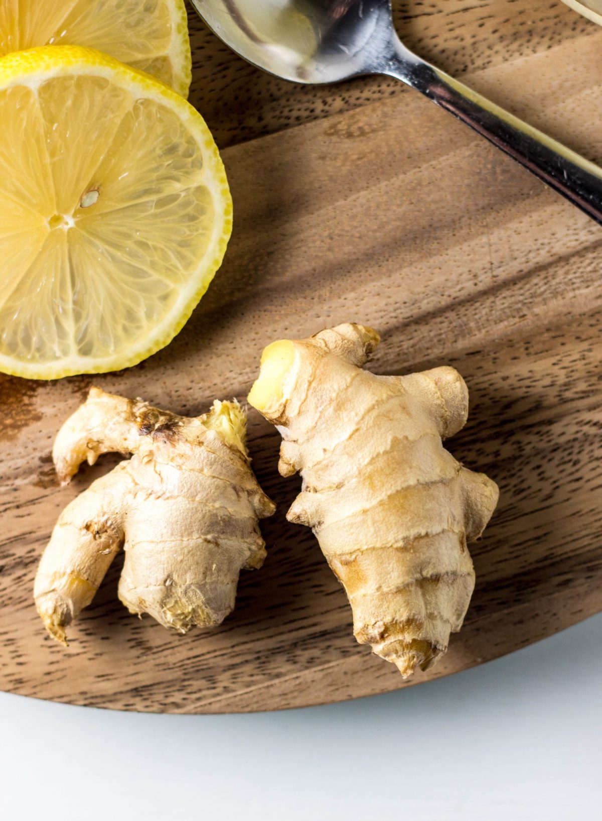 Close up of fresh ginger and lemon slices on a wooden cutting board.