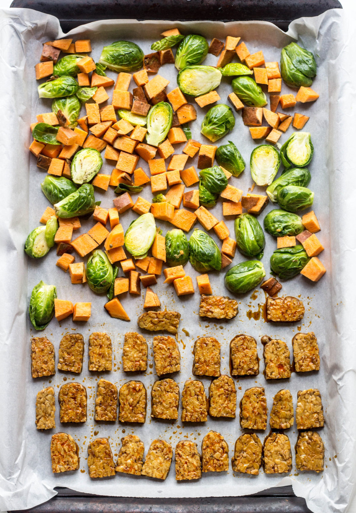 Brussels sprouts halves, sweet potato cubes and marinated tempeh on a baking sheet, top view. 