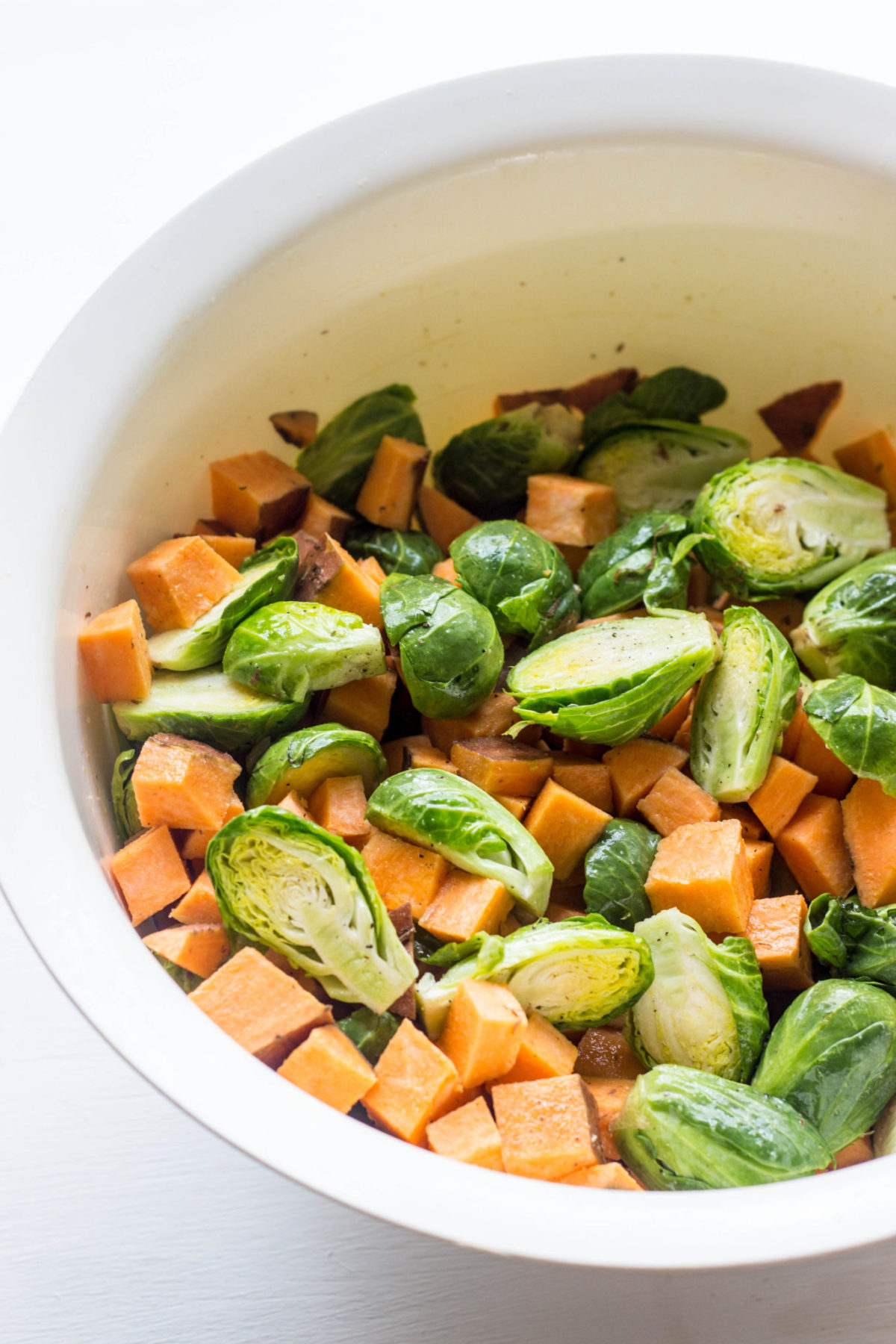 Brussels sprout and cubed sweet potato in a white bowl, 45 degree angle. 