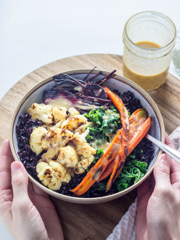 Maple Dijon Roasted Vegetable bowl with hands holding the bowl. 