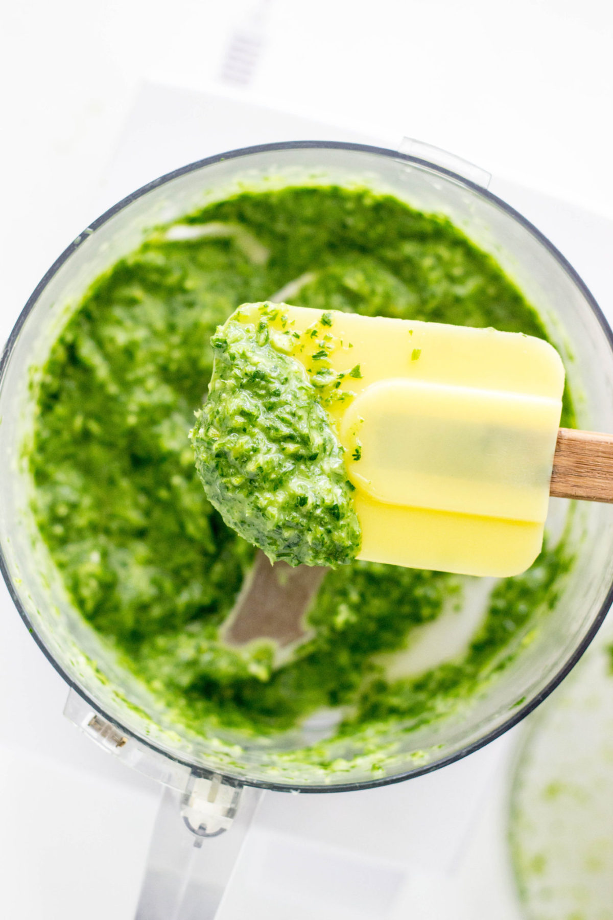 Herb sauce for chickpea Tartine on a rubber spatula above a food processor bowl