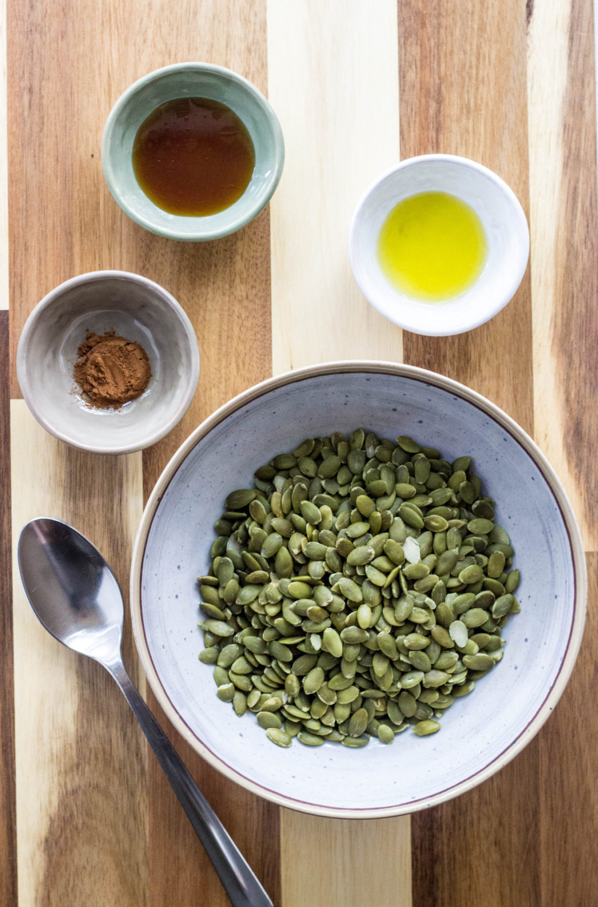 Ingredients in small bowls to make Sweet and Salty Pumpkin Seeds against a wood background. 