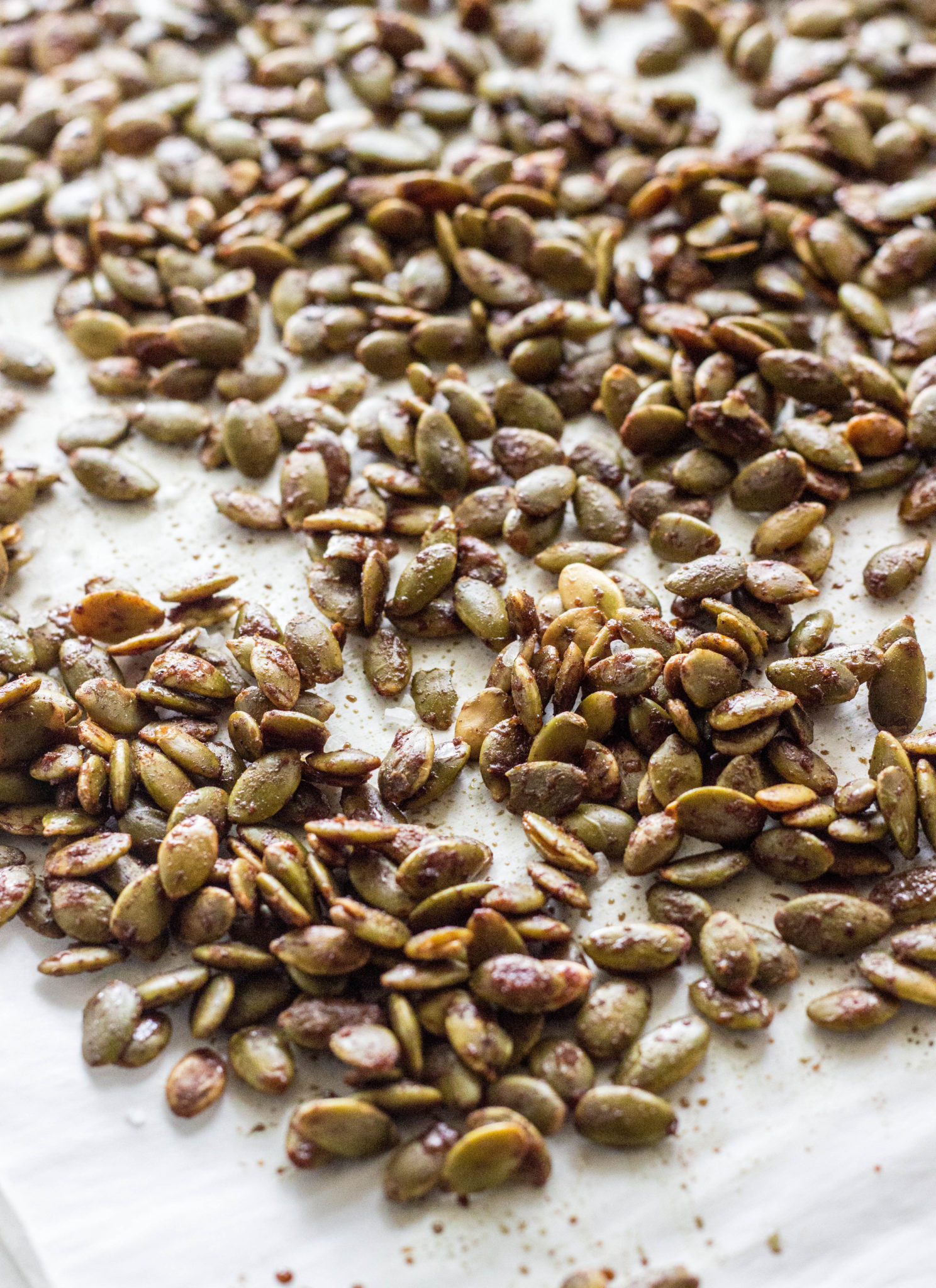 Close up of baked pumpkin seeds on a parchment lined baking sheet. 