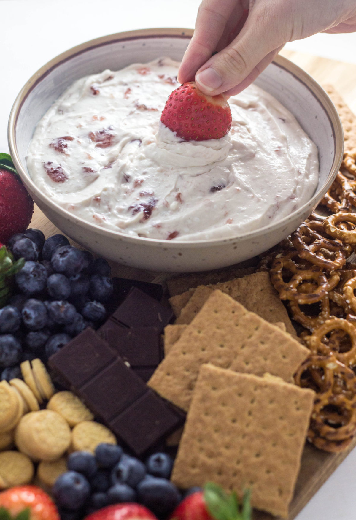 Side view of yogurt dip charcuterie board with hand dipping strawberry into dip. 