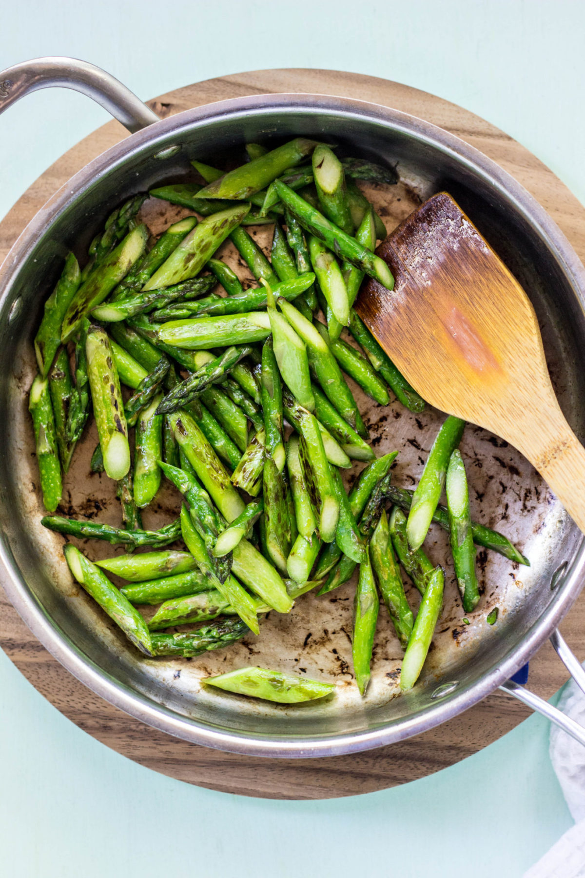 Overhead view of blistered asparagus  in a stainless steel skillet. 
