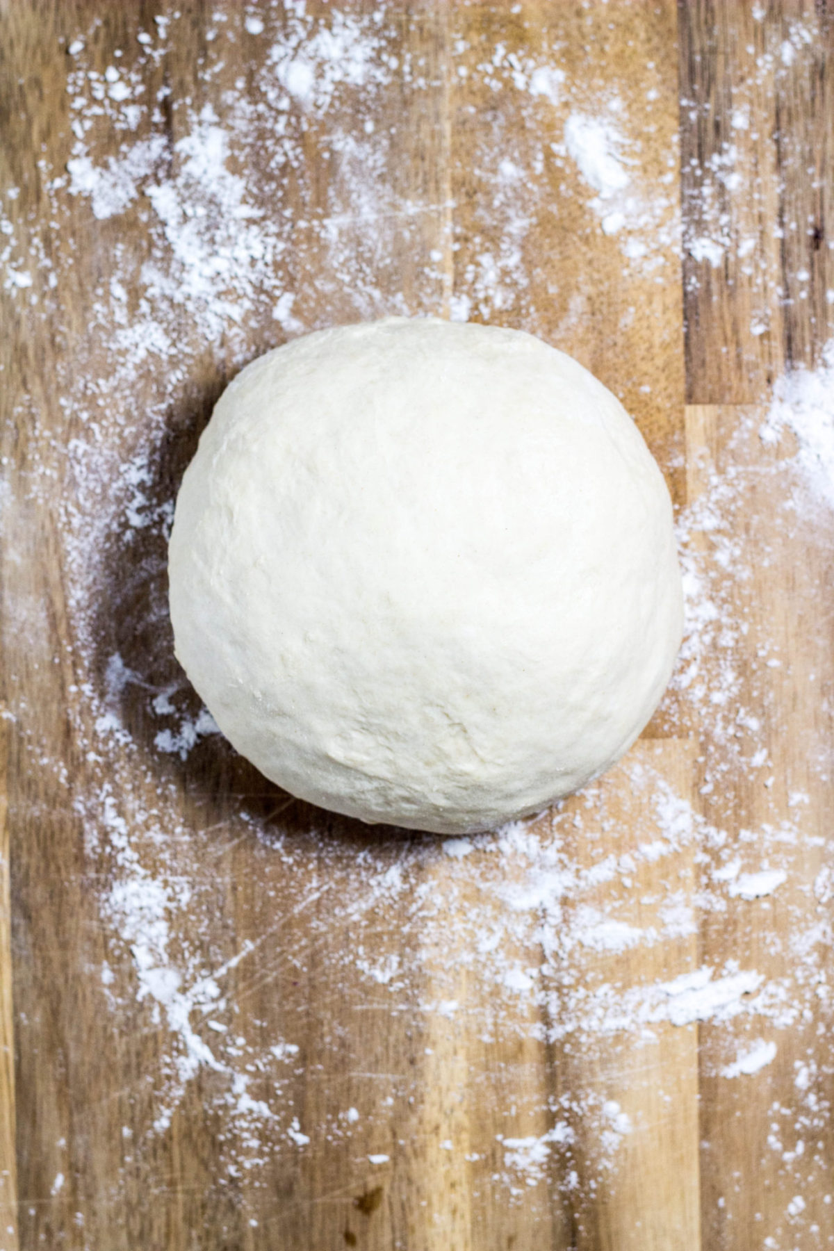 A large dough ball on a floured wooden board. 