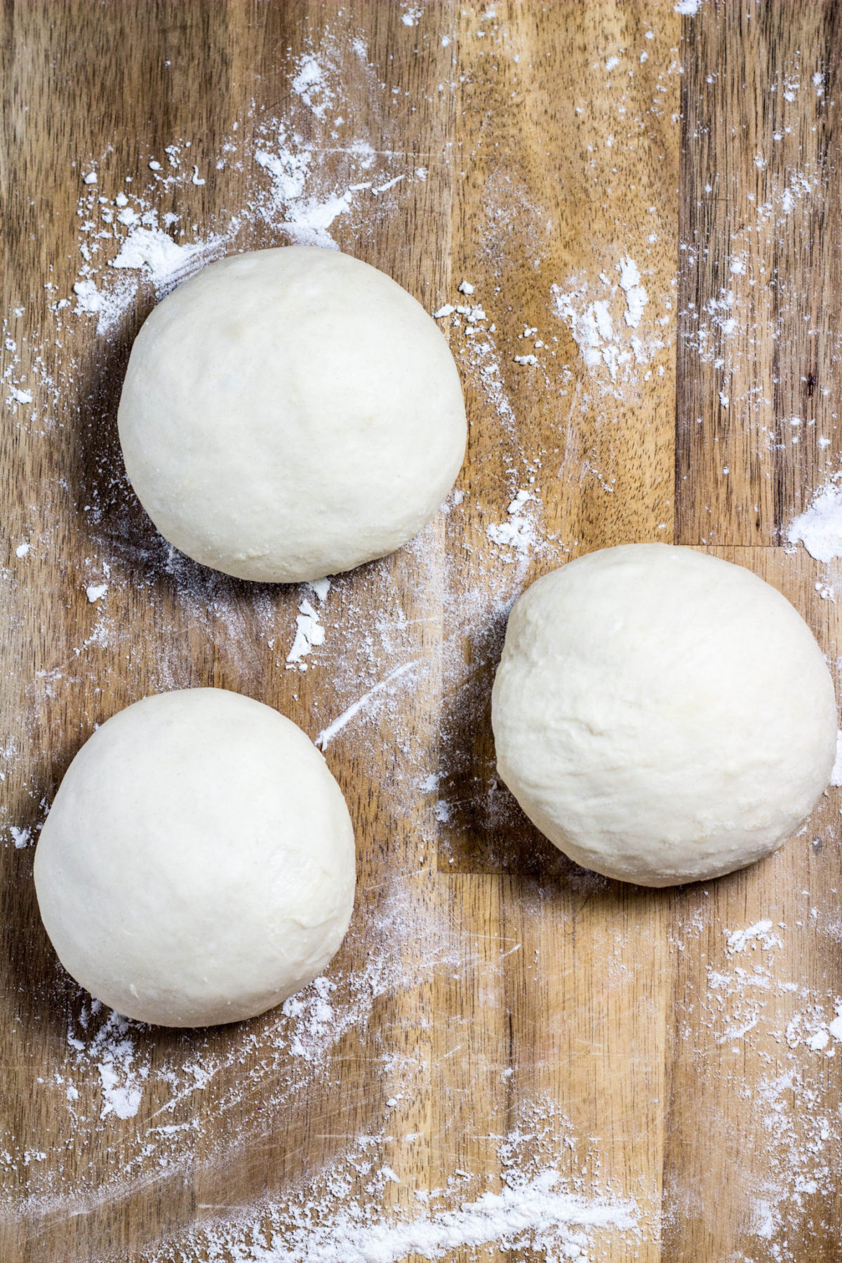 Three small dough balls on a floured wooden board. 