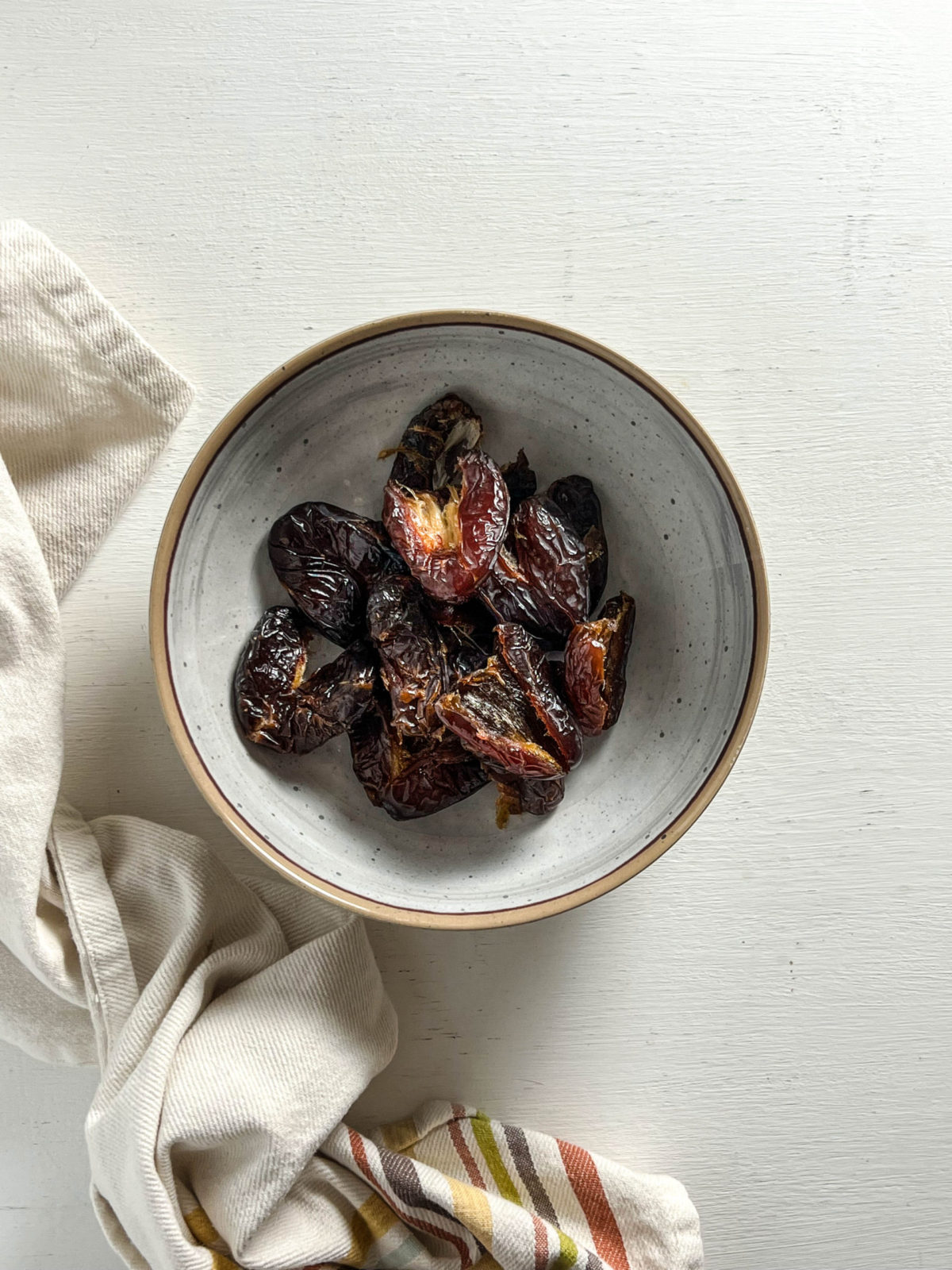 Overhead shot of dates in a bowl with a towel to the side of bowl. 