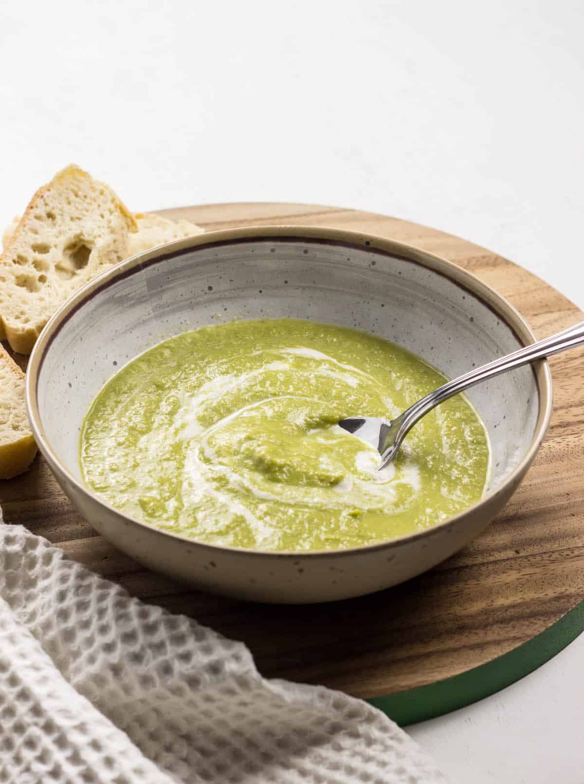 Creamy Asparagus Soup in a bowl on a wooden board with bread to the side.