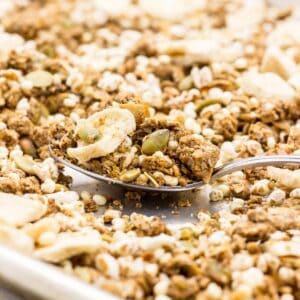 Close up of a spoon of granola resting on a baking sheet of more granola.