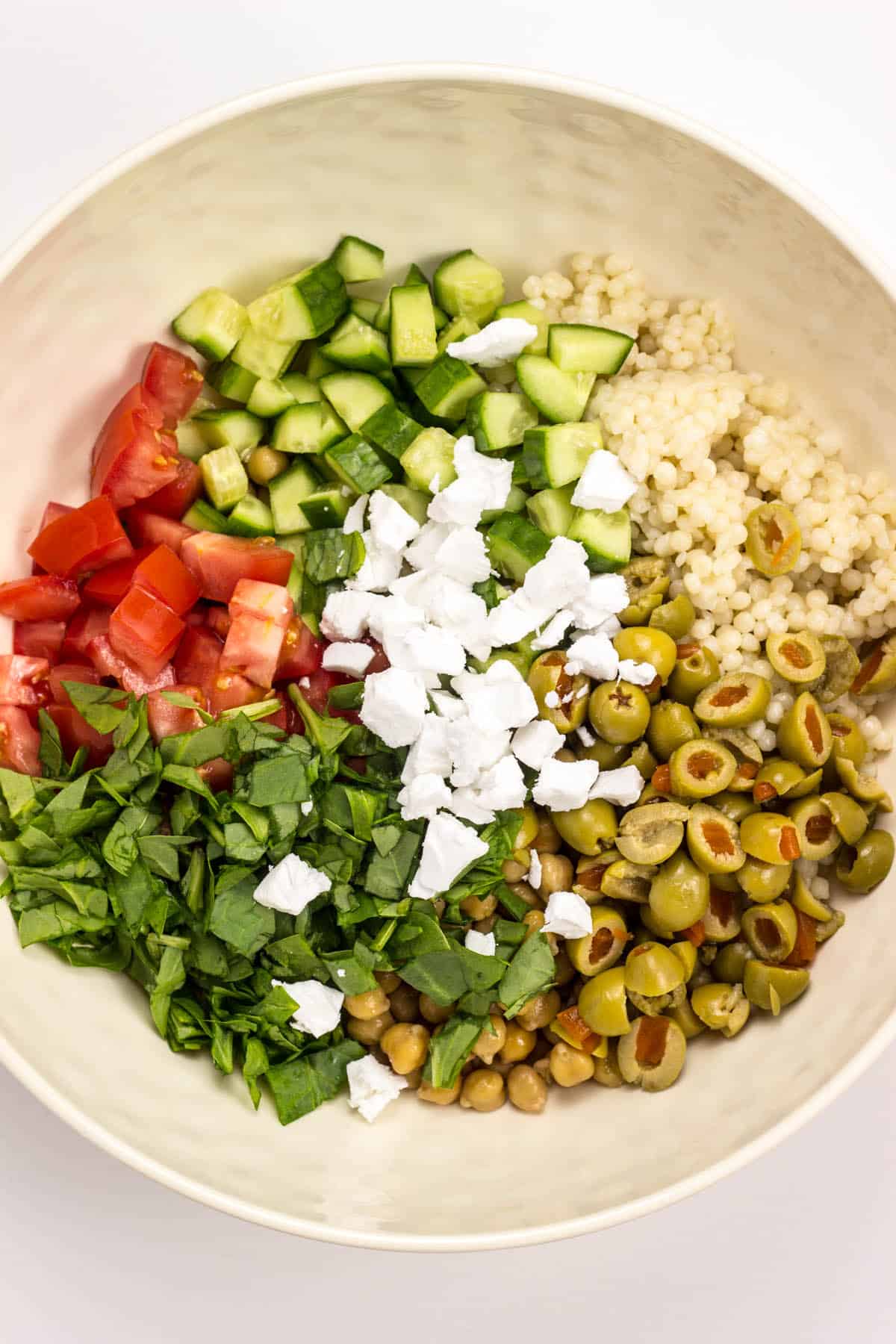 Ingredients for Vegan Mediterranean Couscous Salad in a bowl before being tossed to incorporate.