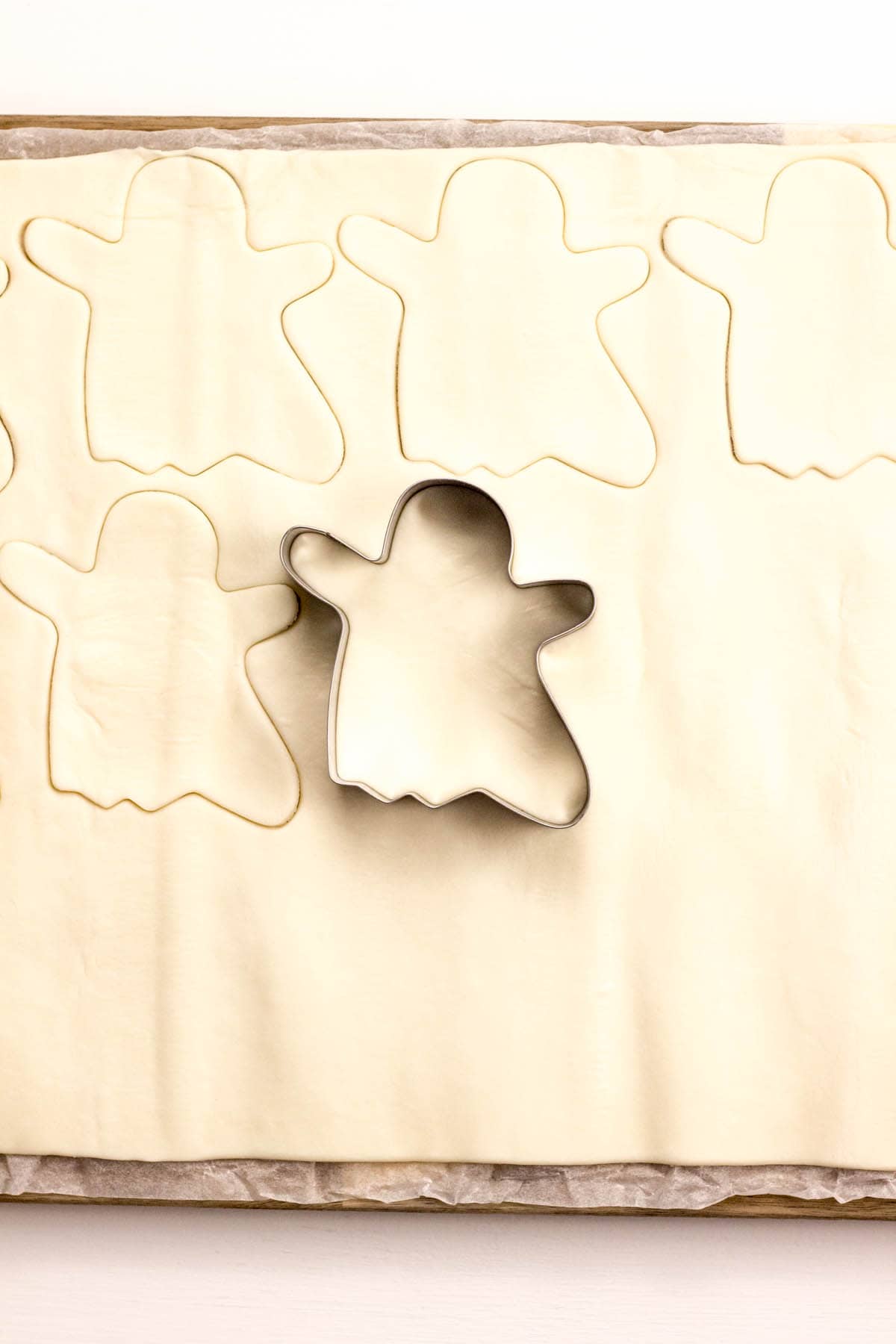 Top view of puff pastry rolled out with a ghost shaped cut outs and a cookie cutter.