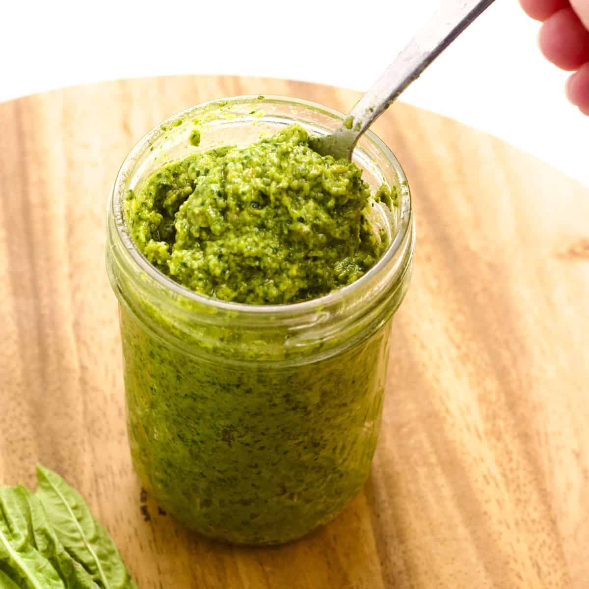 Side view of a jar of Dairy free Pepita Pesto with a spoon.
