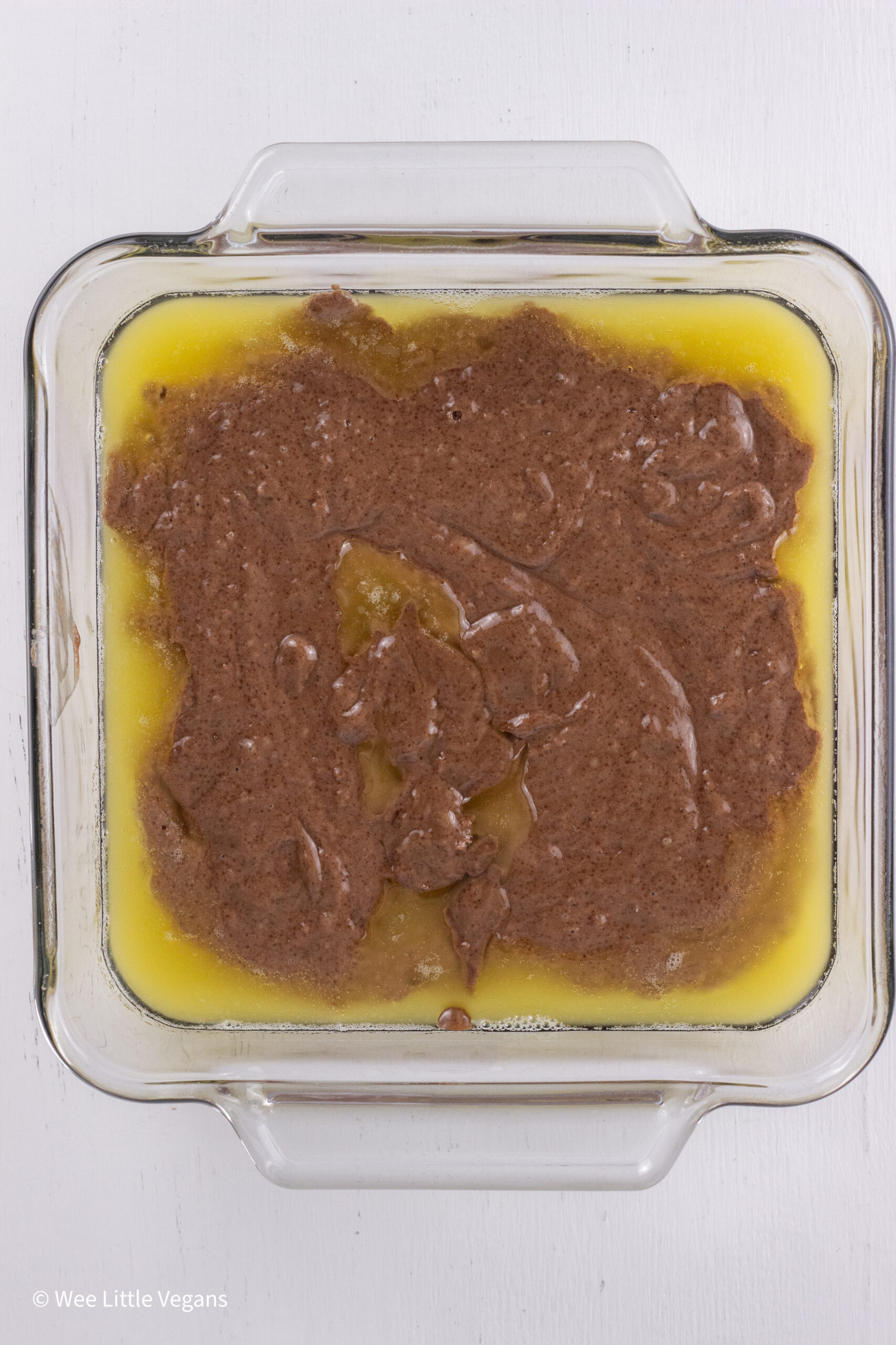 Overhead shot of melted butter and raw batter in a square baking dish.