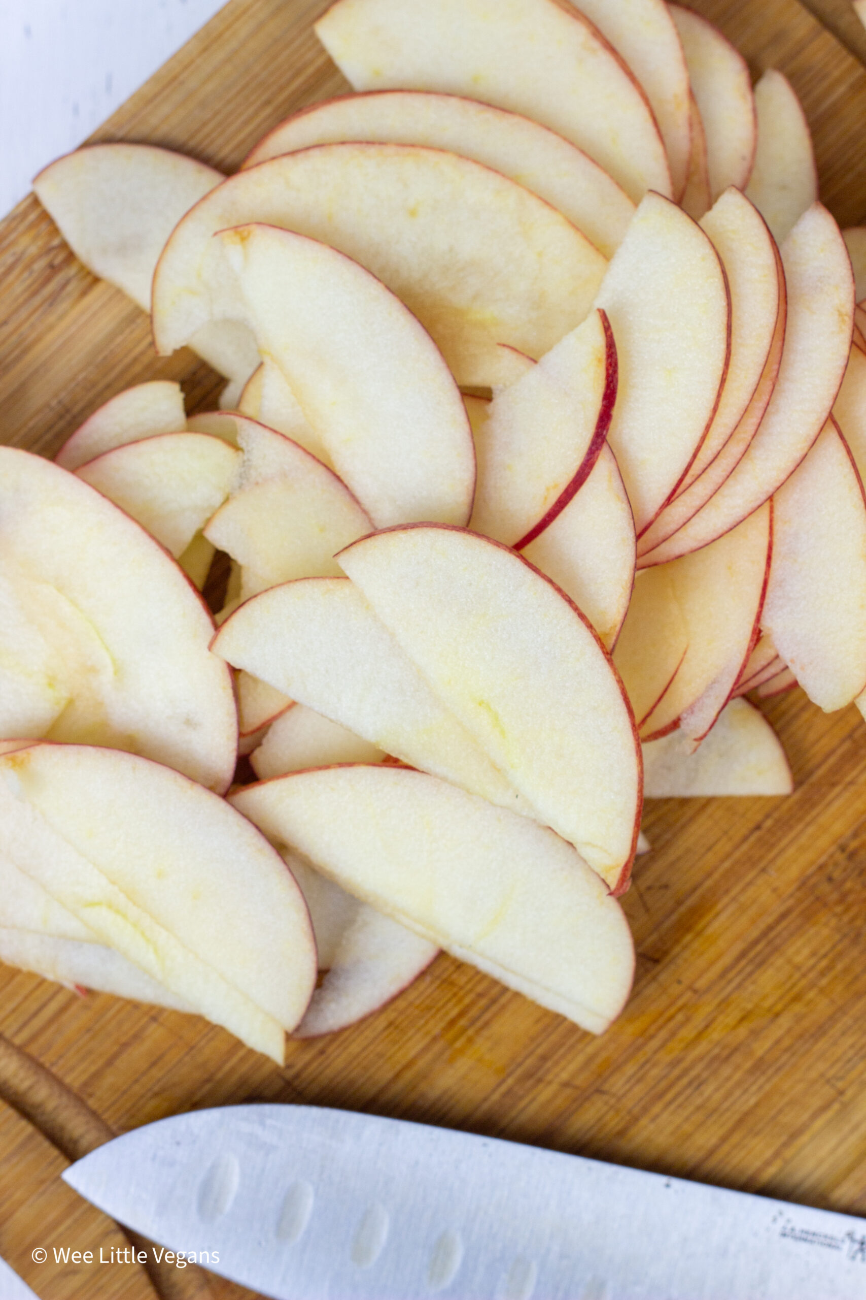 Overhead close up of apples sliced thinly on a cutting board for Apple Pecan Greens Salad. 