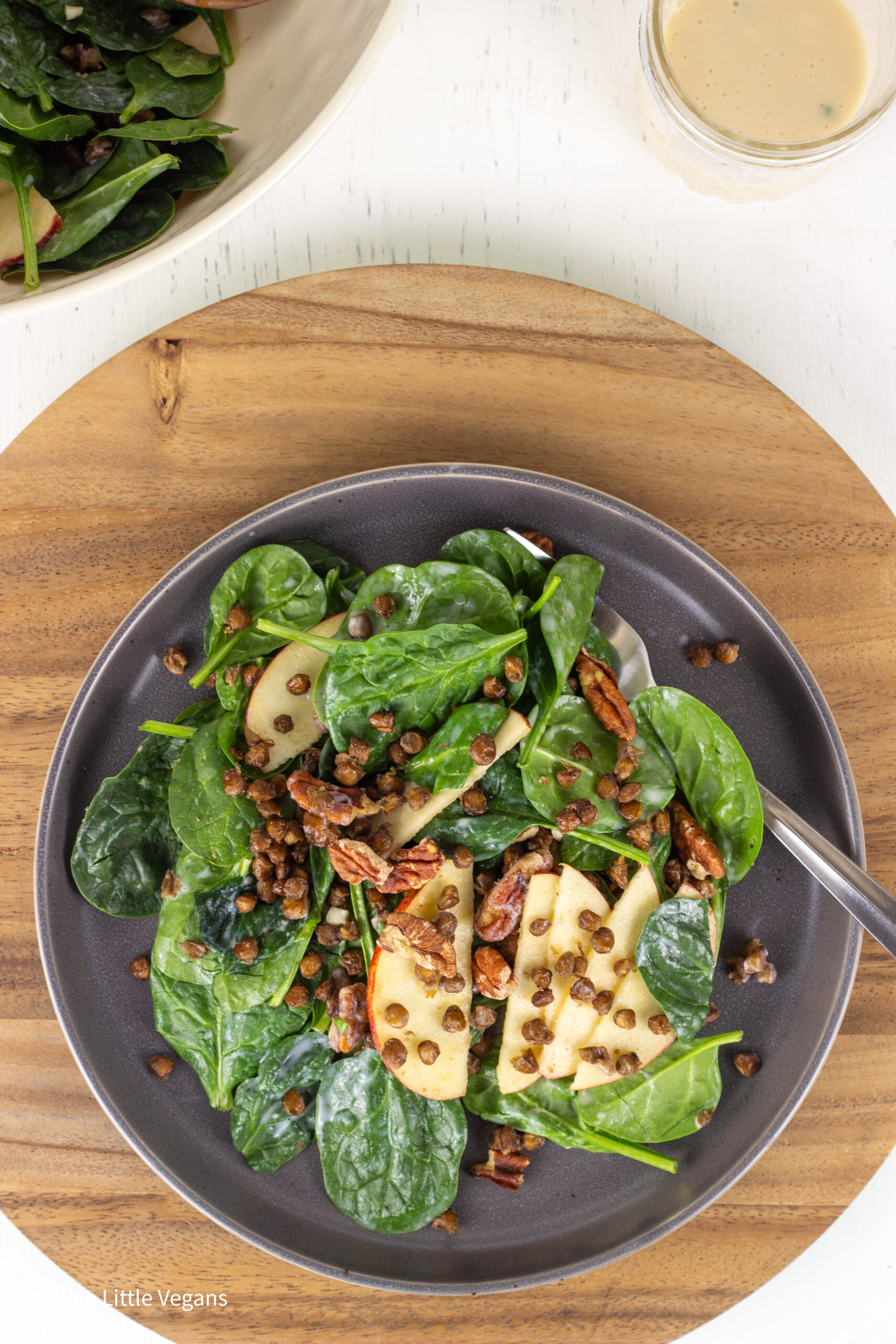 Overhead view of Apple Pecan Greens Salad on a gray plate sitting on a round wooden board.