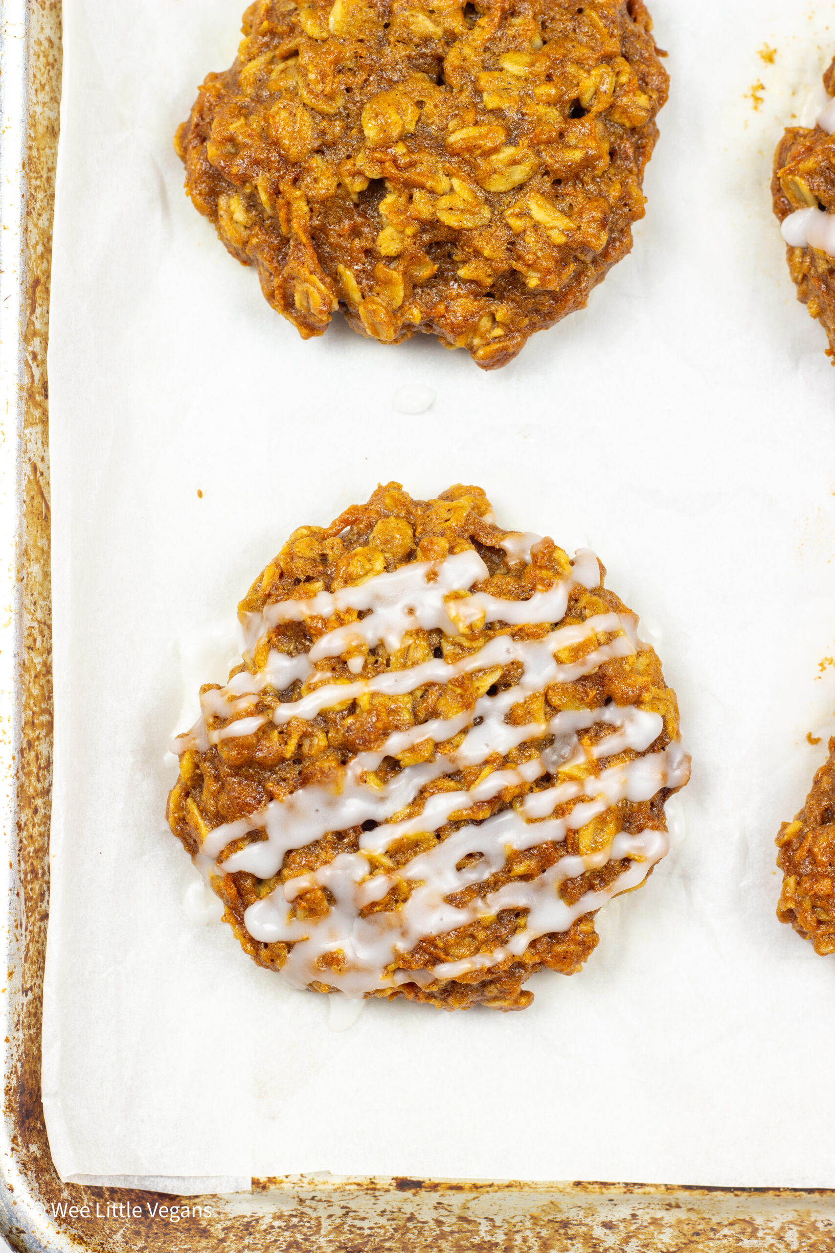 Overhead close up shot of a carrot oatmeal cookie drizzled with glaze on a baking sheet.