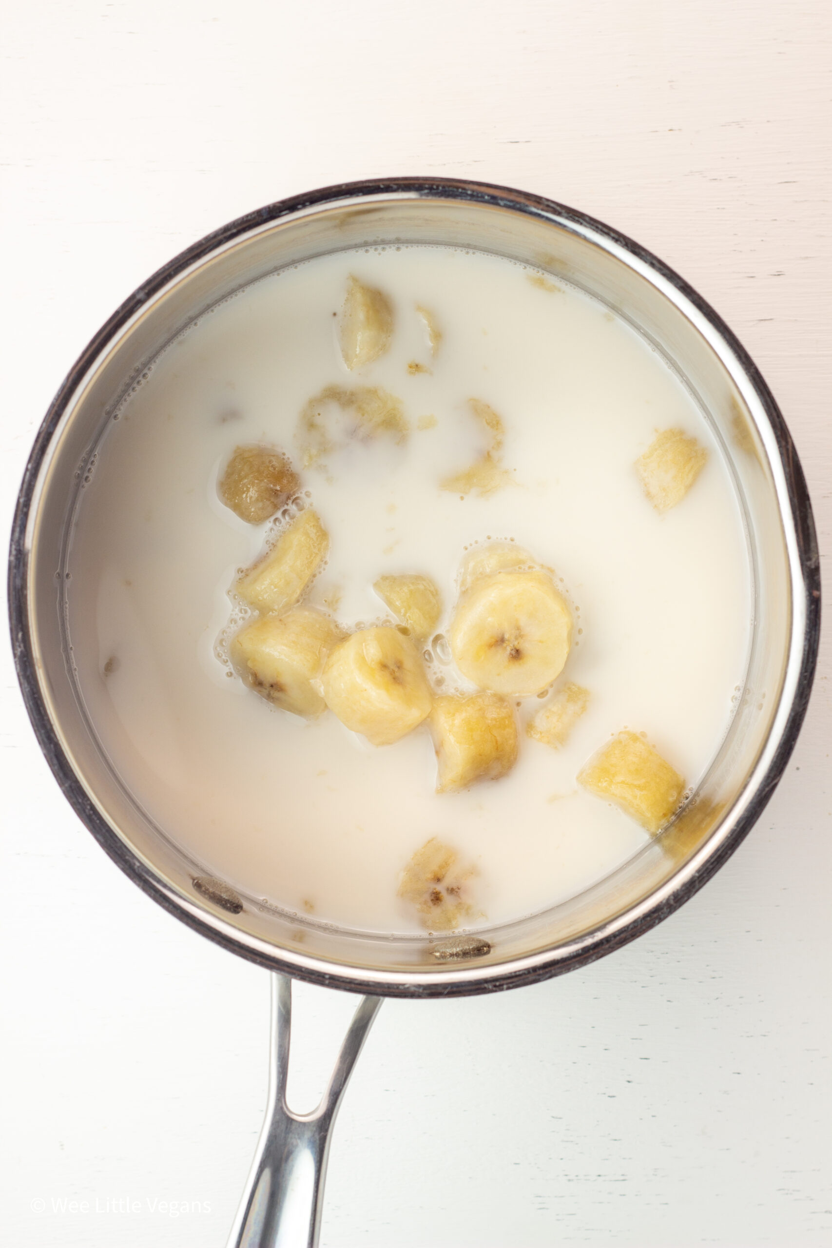 Overhead shot of banana slices and non dairy milk in a sauce pan.