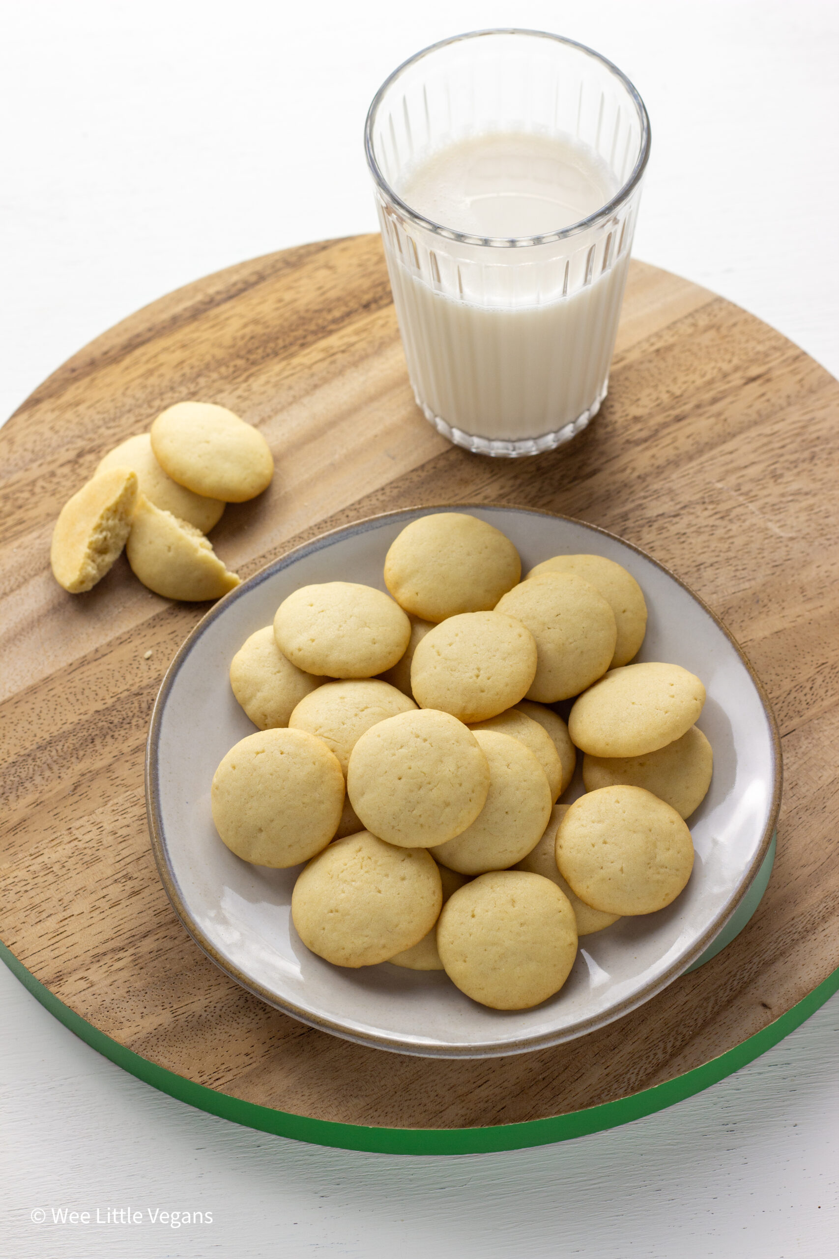 Vegan Vanilla Wafers on a small plate with a glass of milk in the background.