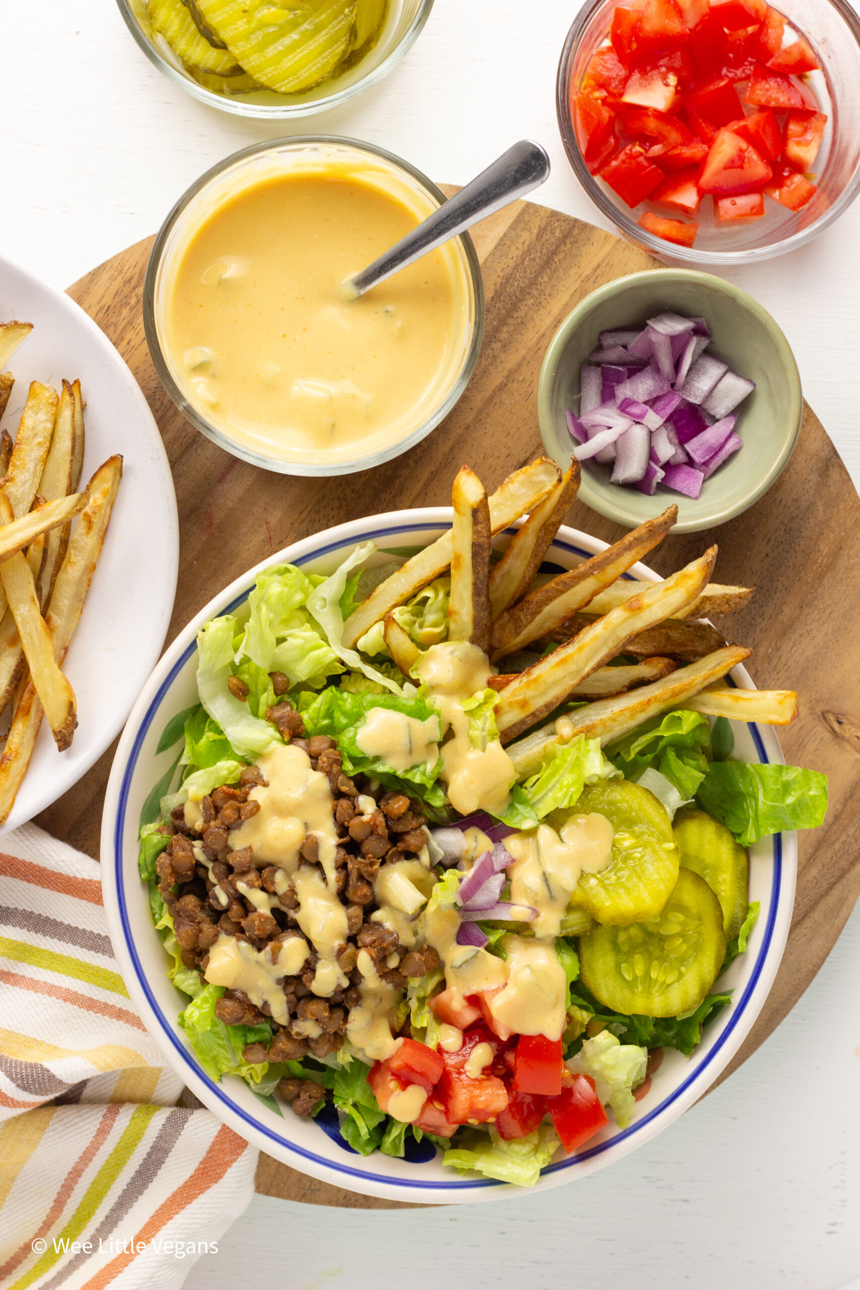 Overhead shot of Vegan Burger Bowl with small bowls of tomato, onion, special sauce and fries to the side.