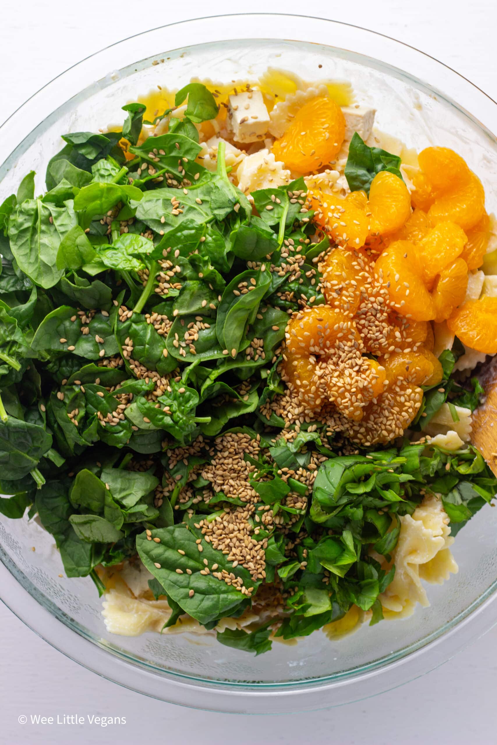 A large bowl of pasta with spinach, mandarin oranges and basil sprinkled with toasted sesame seeds.
