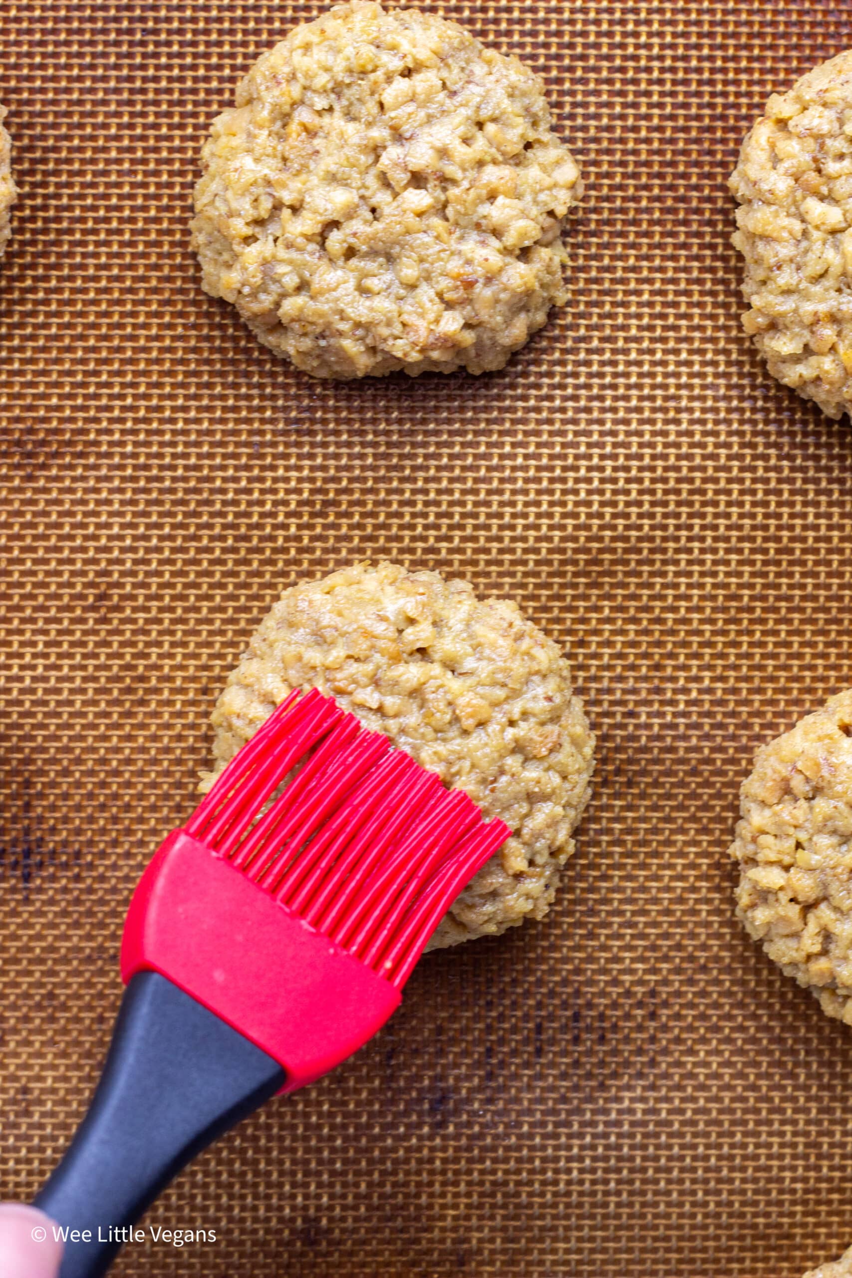 Close up of TVP Breakfast Sausages on a baking sheet being brushed with oil.