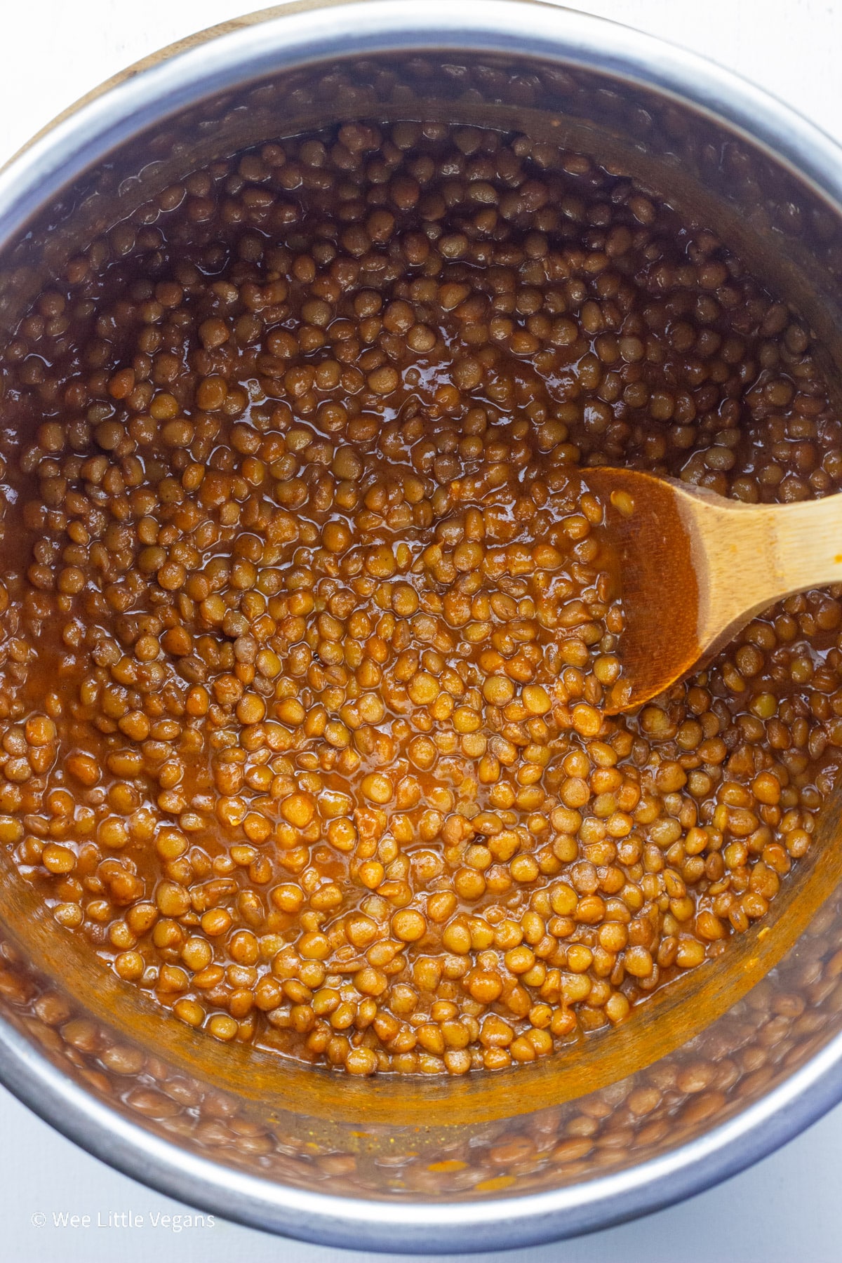 Overhead shot of a pot of Barbecue Lentils with a wooden spoon resting in it.