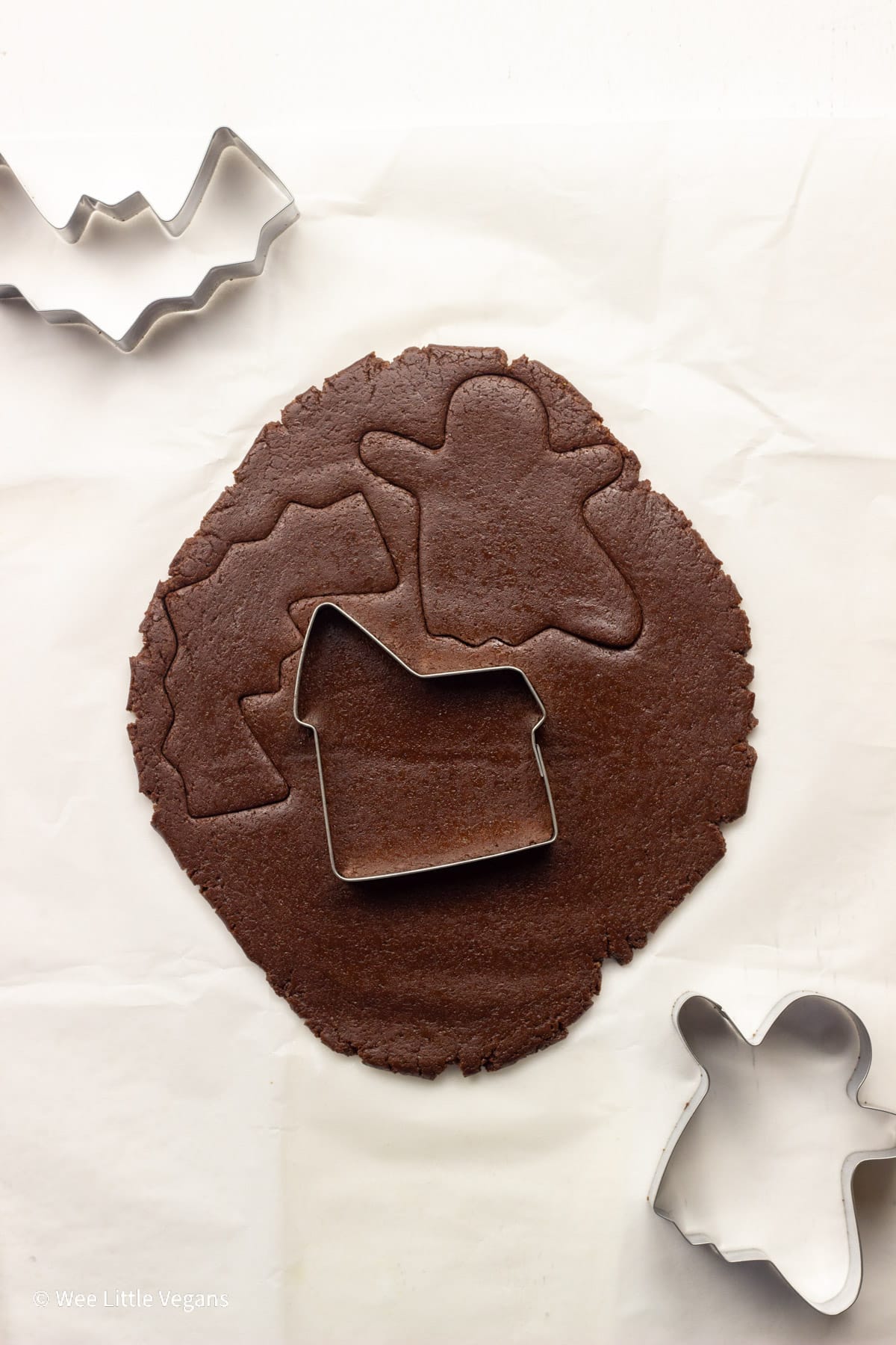 Overhead shot of chocolate cookie dough rolled out on parchment paper with cookie cutters.