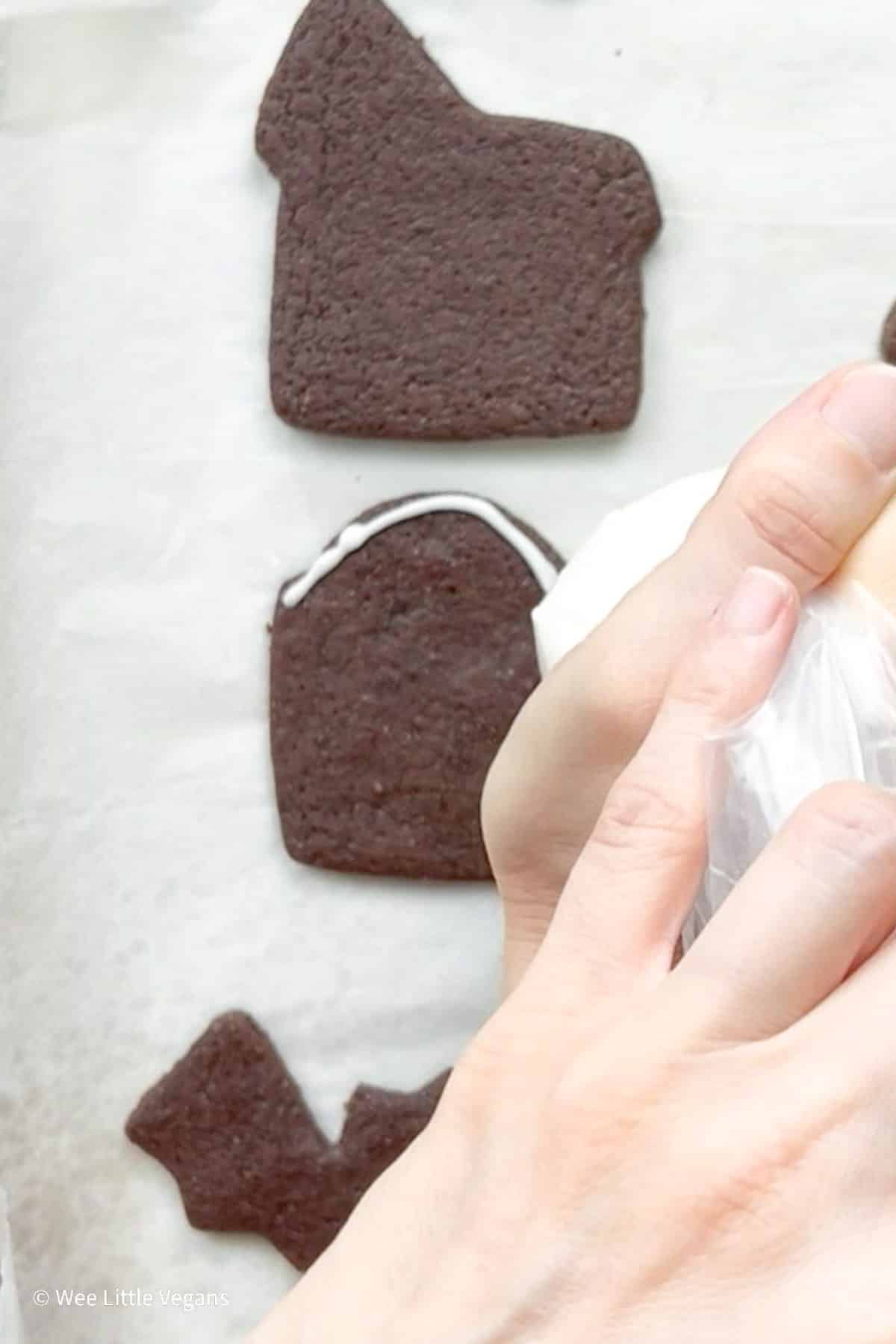 Overhead shot of hands piping frosting on to Halloween themed chocolate cookies on a baking sheet.