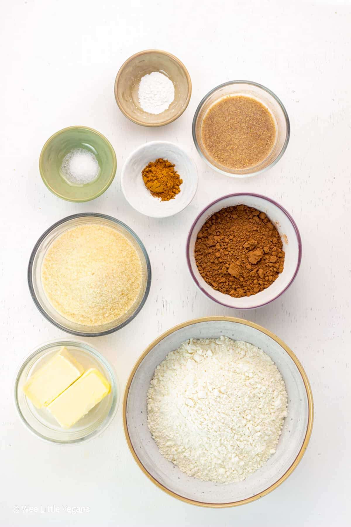Overhead shot of ingredients to make Spiced Chocolate Cut Out Cookies. Flour, non dairy butter, cocoa powder, sugar, flax egg, pumpkin pie spice, salt and baking powder in individual bowls.
