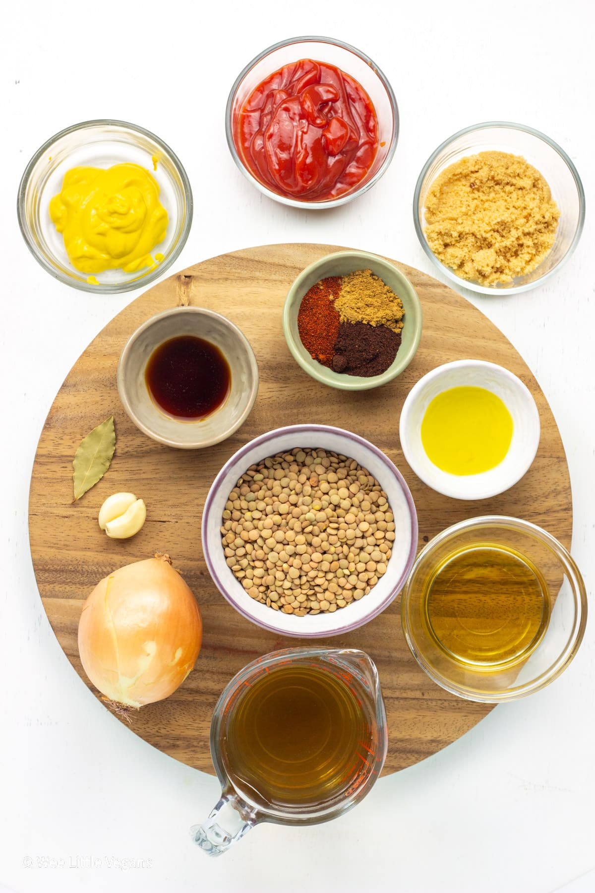 Overhead shot of ingredients needed to make Barbecue Lentils. Dry lentils, onion, garlic, bay leaf, broth, apple cider vinegar, oil, spices, brown sugar, ketchup, mustard and liquid smoke.