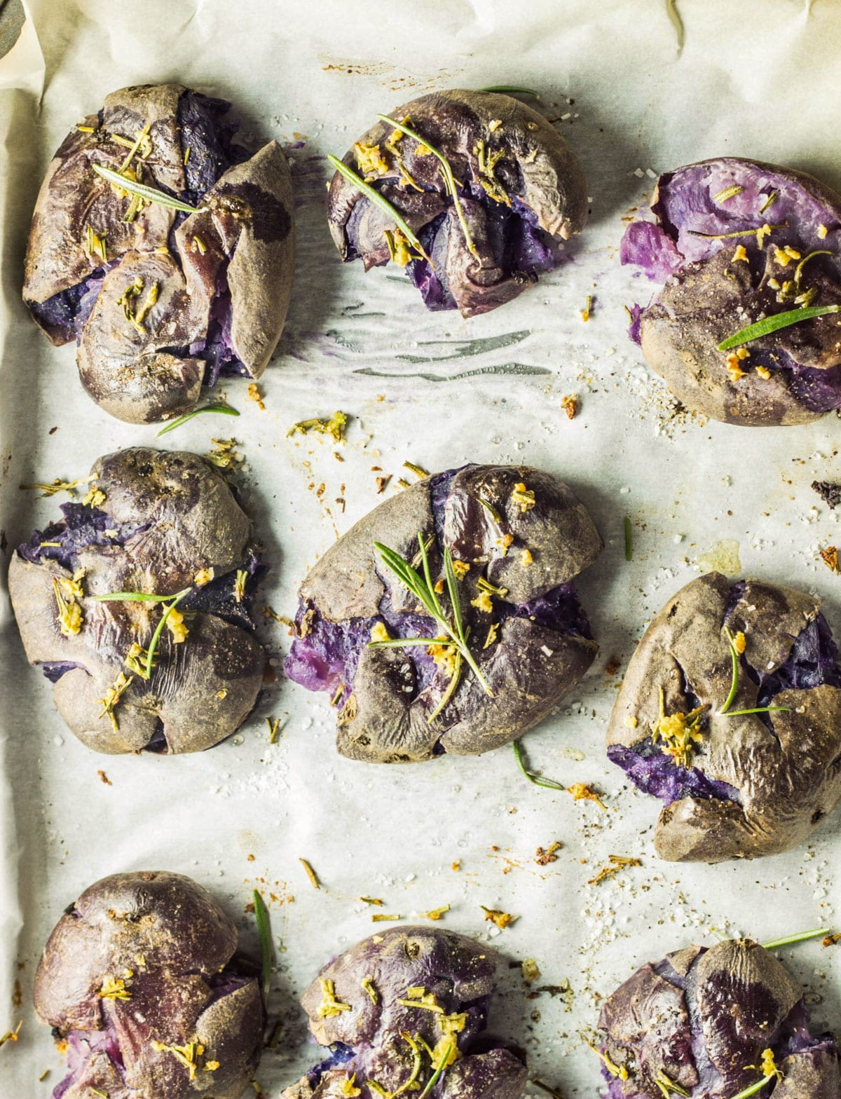 Overhead shot of Garlic Rosemary Smashed Purple Potatoes on a baking sheet.