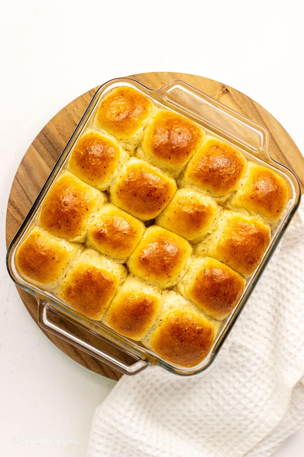 Overhead view of a baking dish of Vegan Hawaiian Rolls. There is a white towel to the side of the dish.