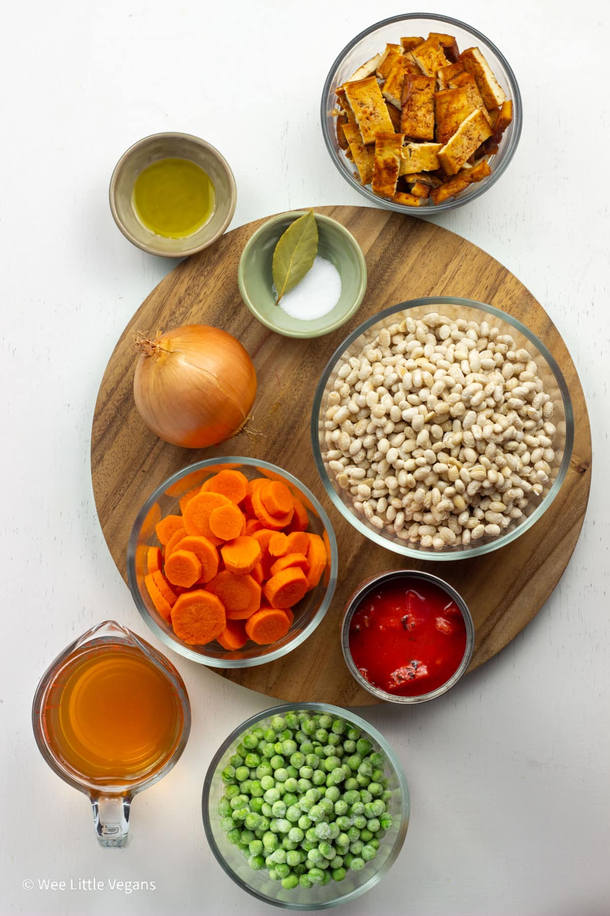 Overhead view of ingredients to make Vegan Navy Bean Soup. Dry navy beans, diced tomatoes, carrots, peas, broth, onion, bay leaf, oil, tofu bacon and salt.
