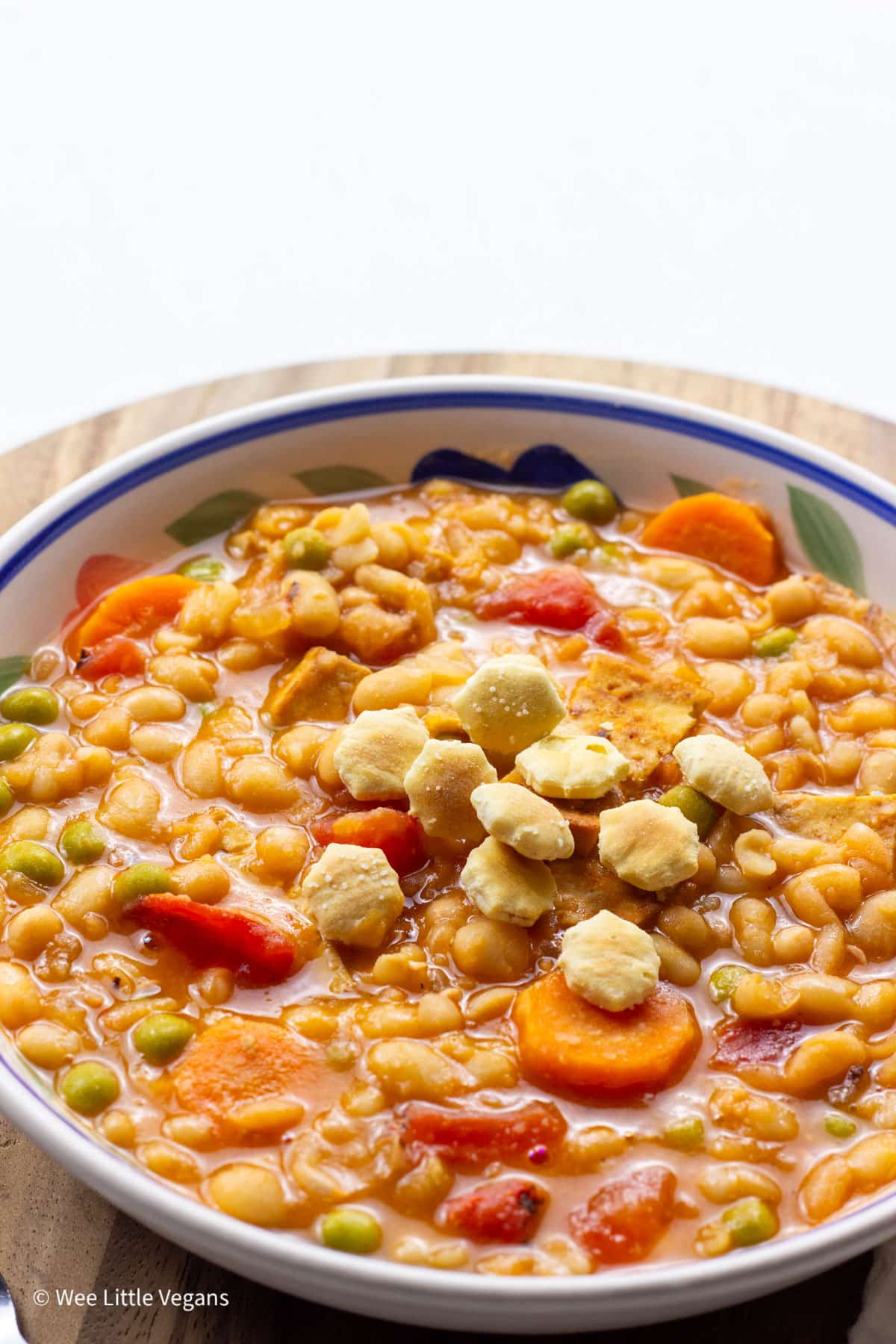 Close up side view of a bowl of Vegan Navy Bean Soup. There are small crackers on the top of the soup.