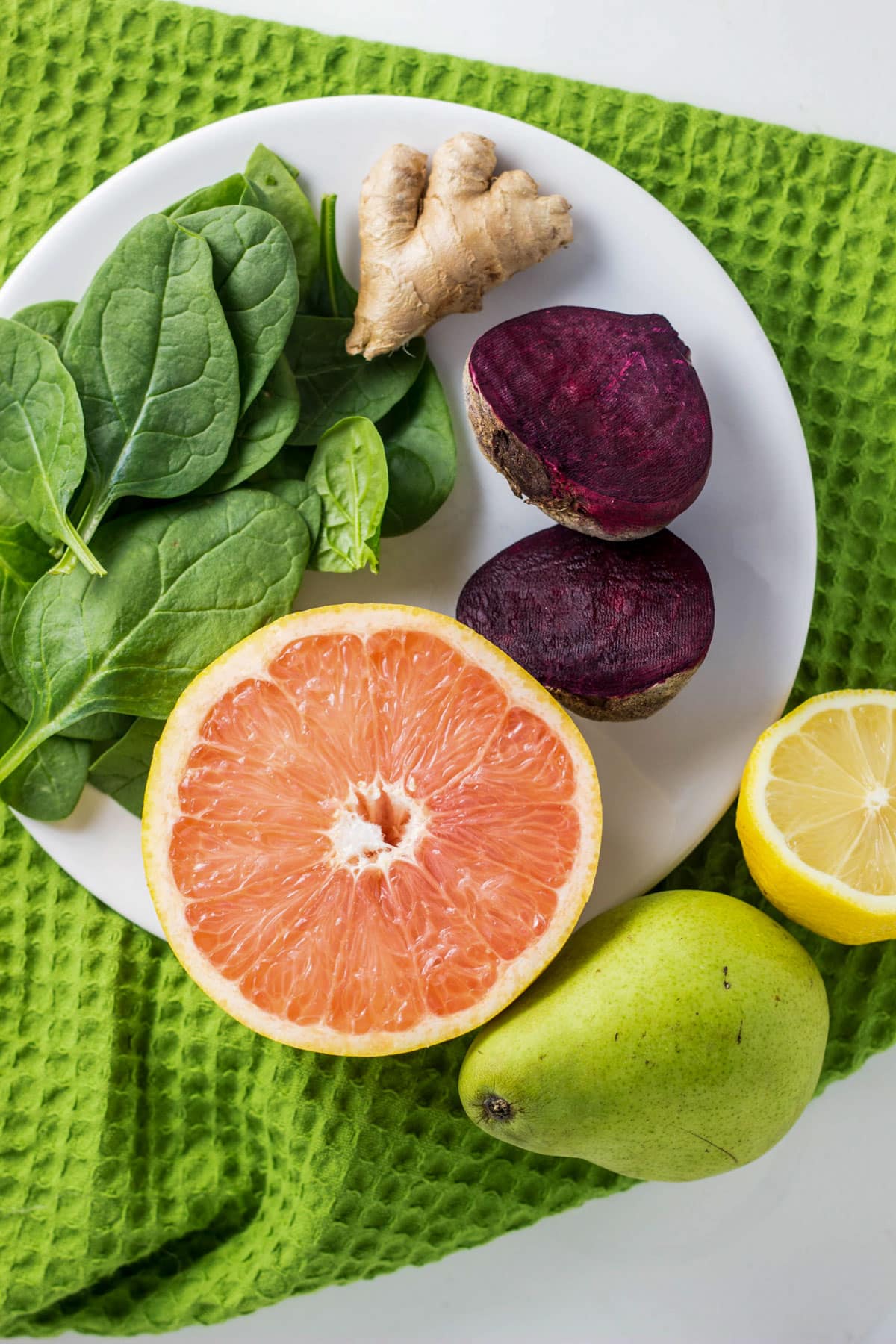 Overhead shot of ingredients for Beet Citrus Smoothie. There is a grapefruit, pear, lemon, spinach, ginger and beet.