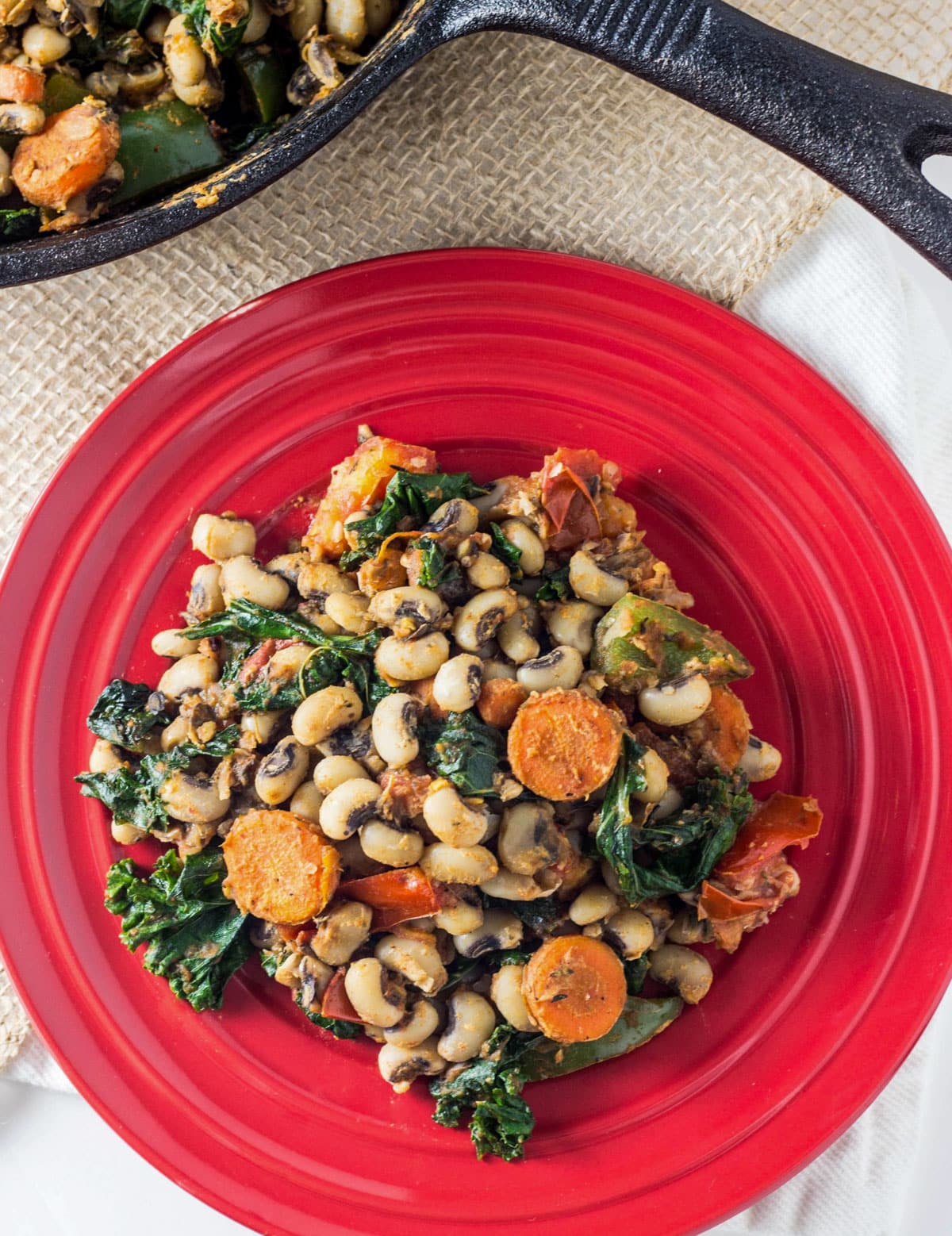 Overhead shot of Black Eye Pea Hash on a small red plate. A cast iron skillet is slightly visible in the frame.