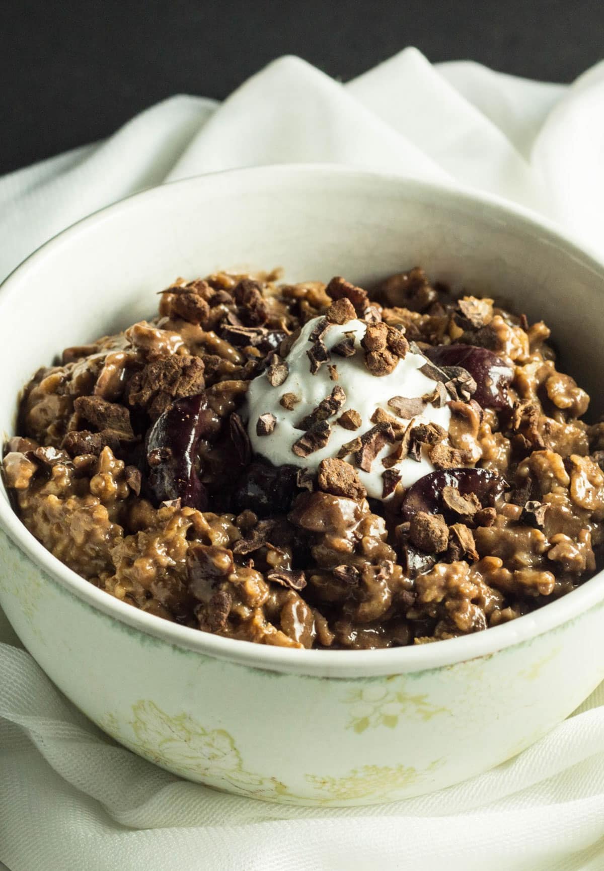 A close up side view of a bowl of Black Forest Cake Oatmeal. The oatmeal is topped with nondairy whipped cream and cacao nibs.